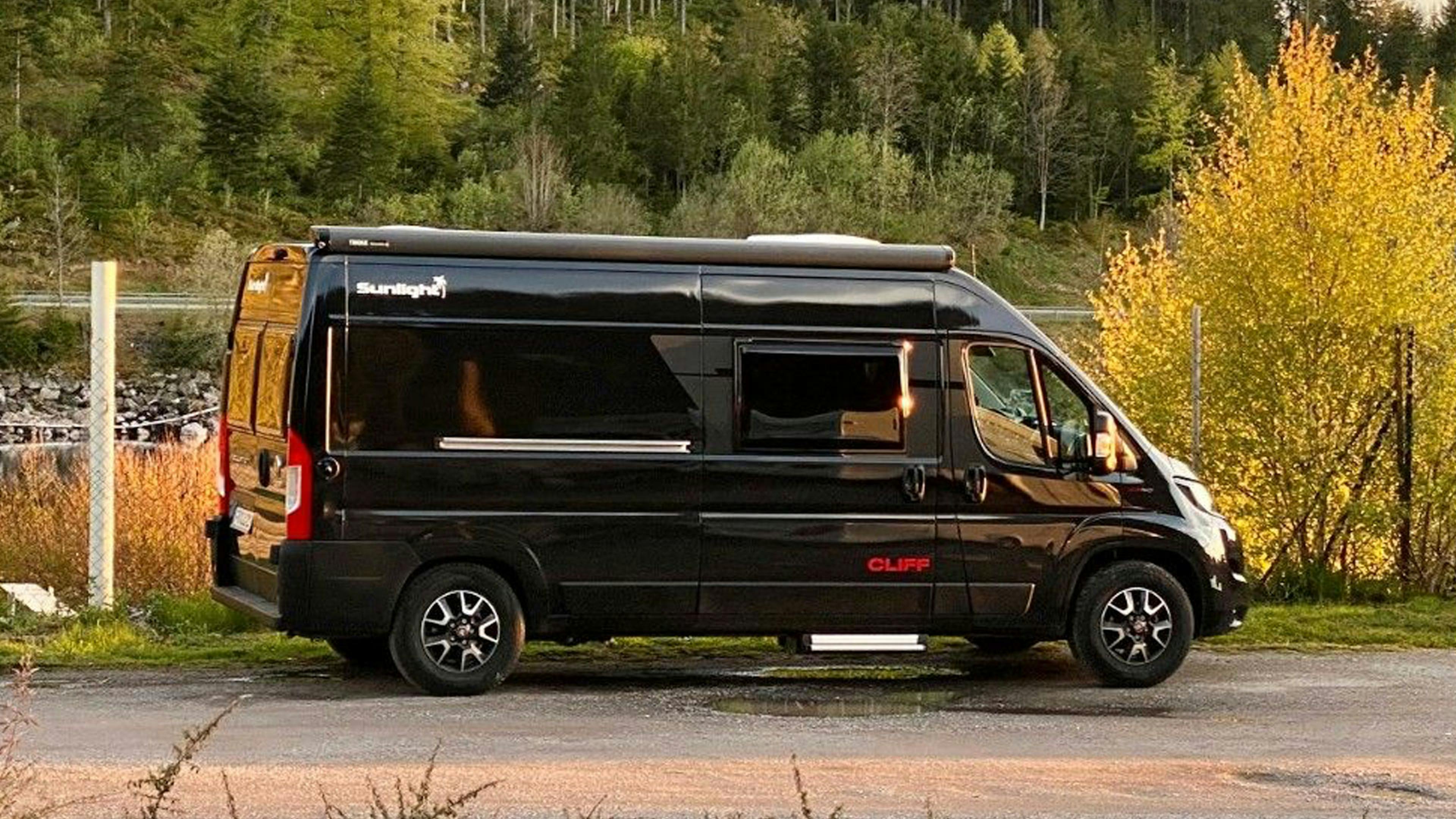 Ein weißes Sunlight Cliff Wohnmobil steht am Rand einer Straße vor einem Waldstück.