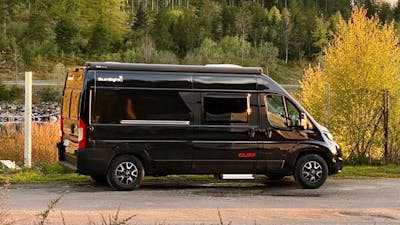 Ein weißes Sunlight Cliff Wohnmobil steht am Rand einer Straße vor einem Waldstück.