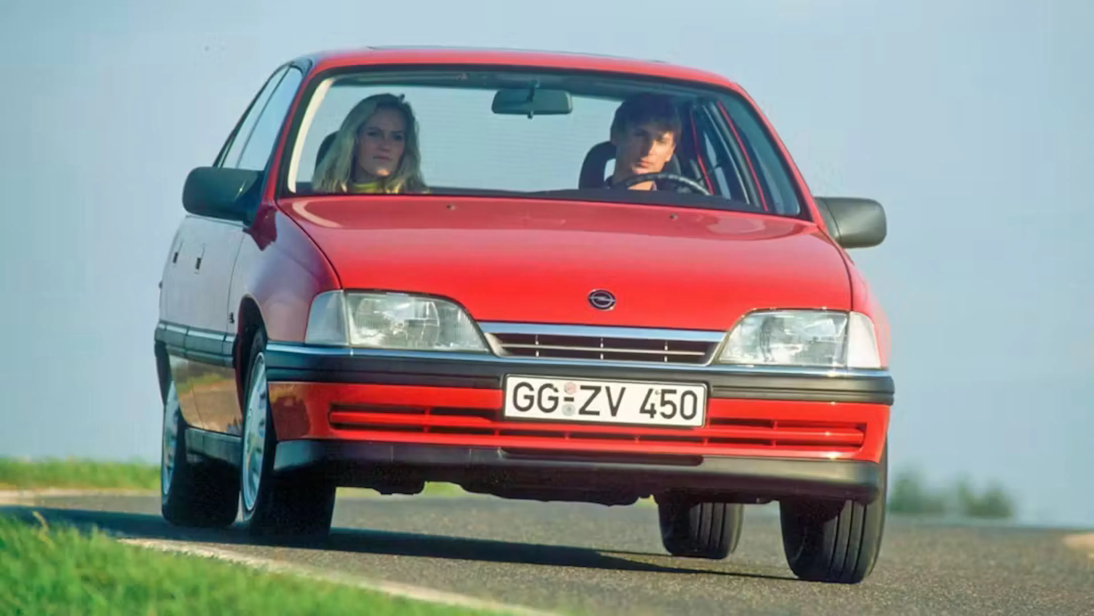Ein roter Opel Omega A fährt auf einer Landstraße.