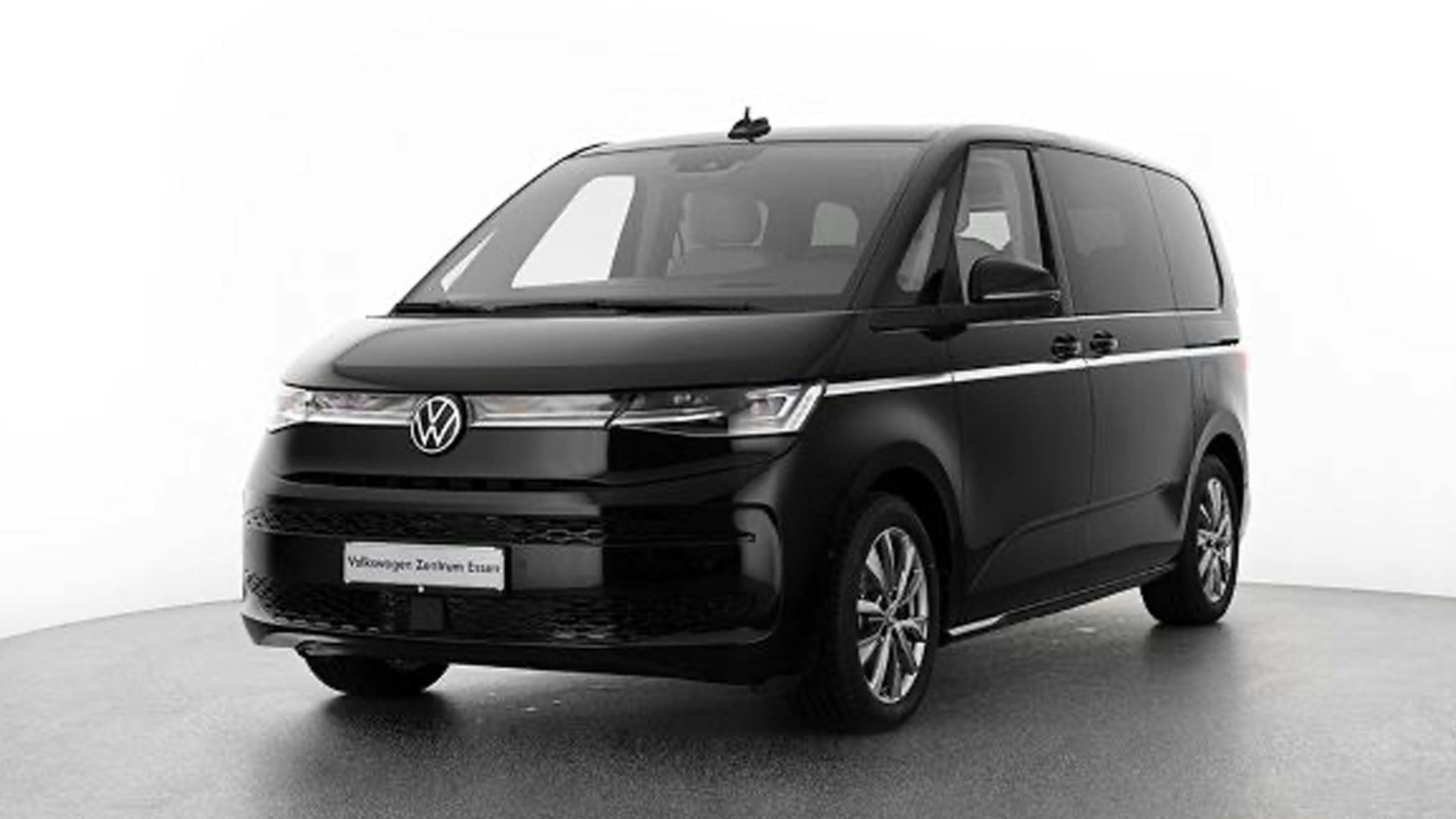 Ein schwarzer VW T7 eHybrid Multivan steht vor einer weißen Wand.