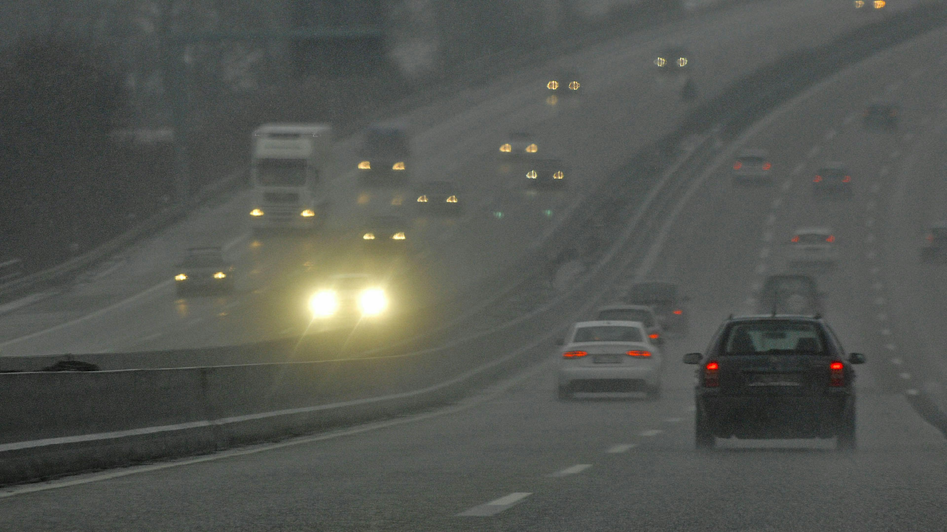 Blick auf eine Autobahn mit mehreren Pkw, von denen einer das Fernlicht eingeschaltet hat.