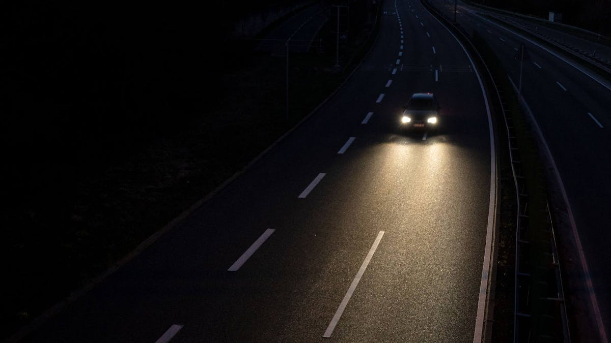 Ein Auto mit eingeschaltetem Fernlicht fährt nachts eine Straße entlang.