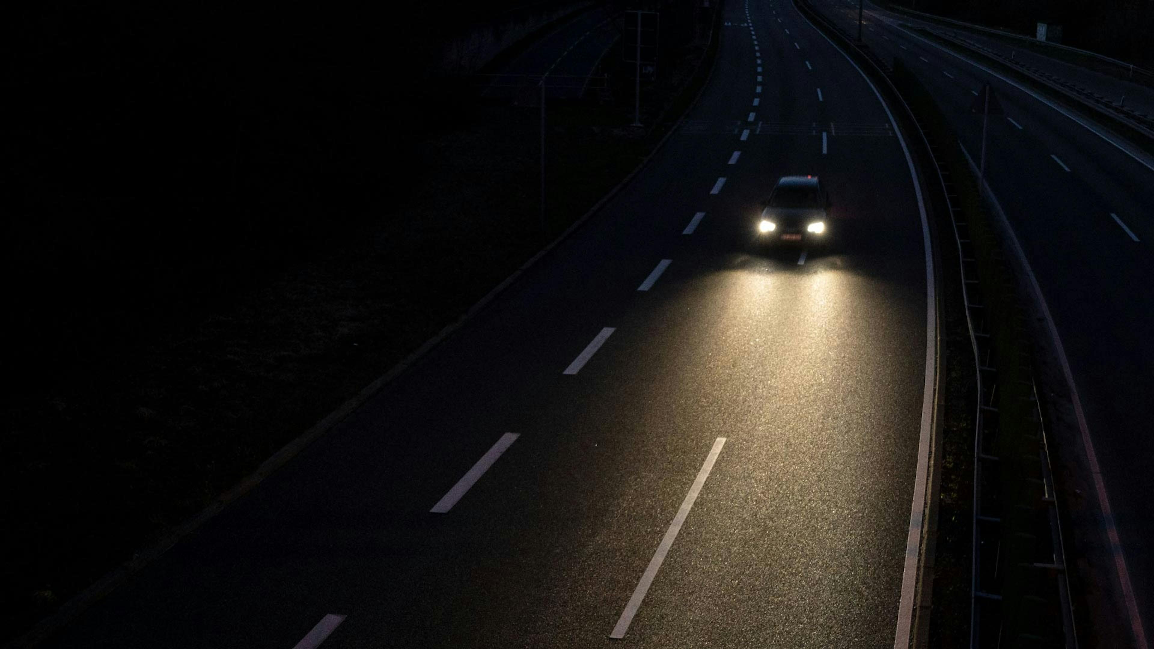 Ein Auto mit eingeschaltetem Fernlicht fährt nachts eine Straße entlang.