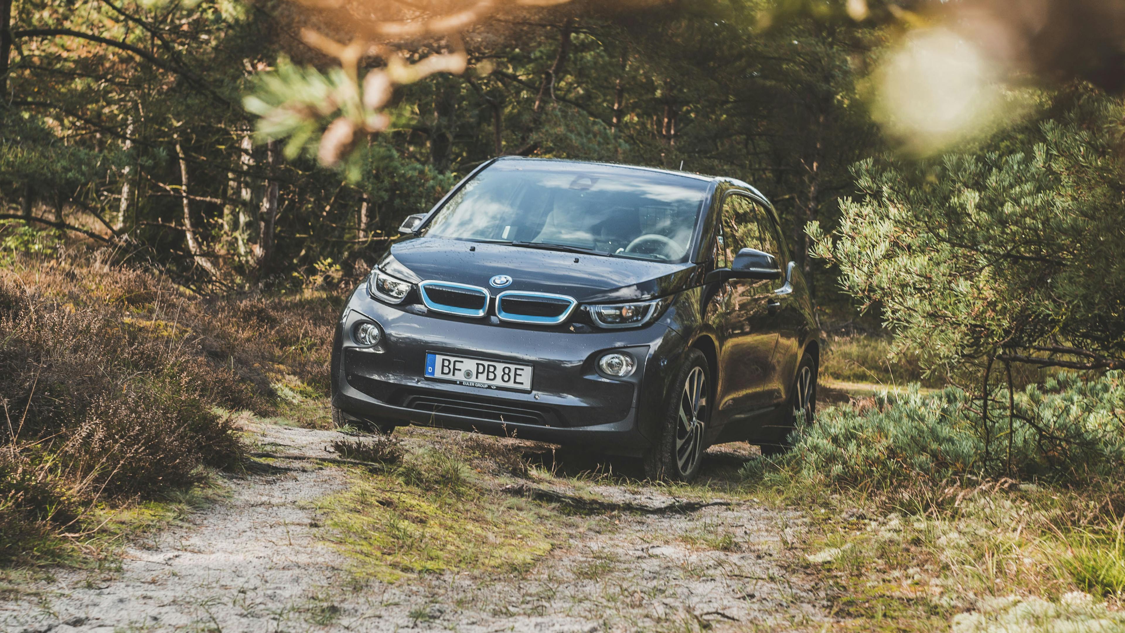 A black BMW i3 is parked in a forest