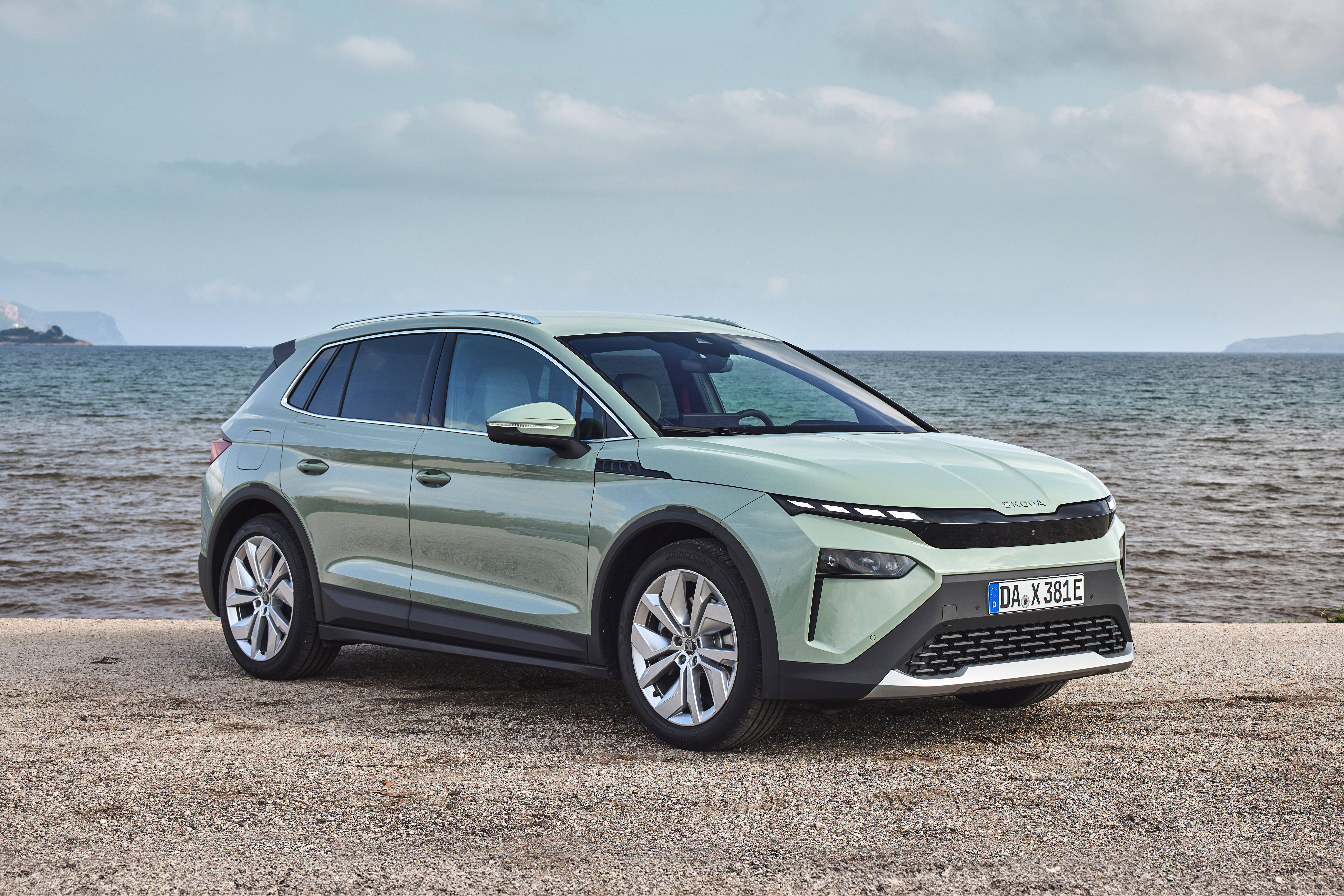 Mintgrüner Škoda Elroq steht auf einem Kiesstrand vor dem Meer.