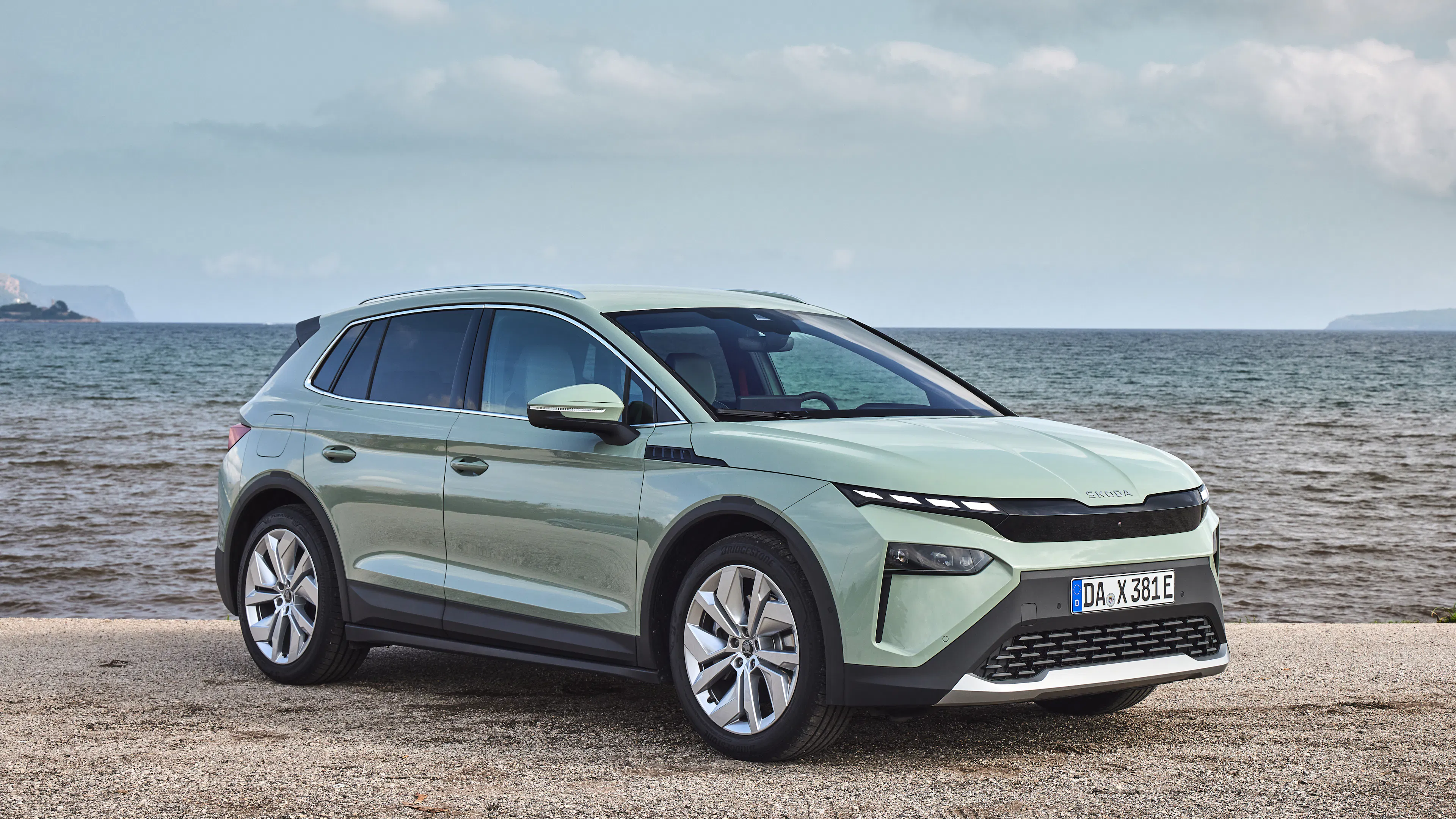 Mintgrüner Škoda Elroq steht auf einem Kiesstrand vor dem Meer.