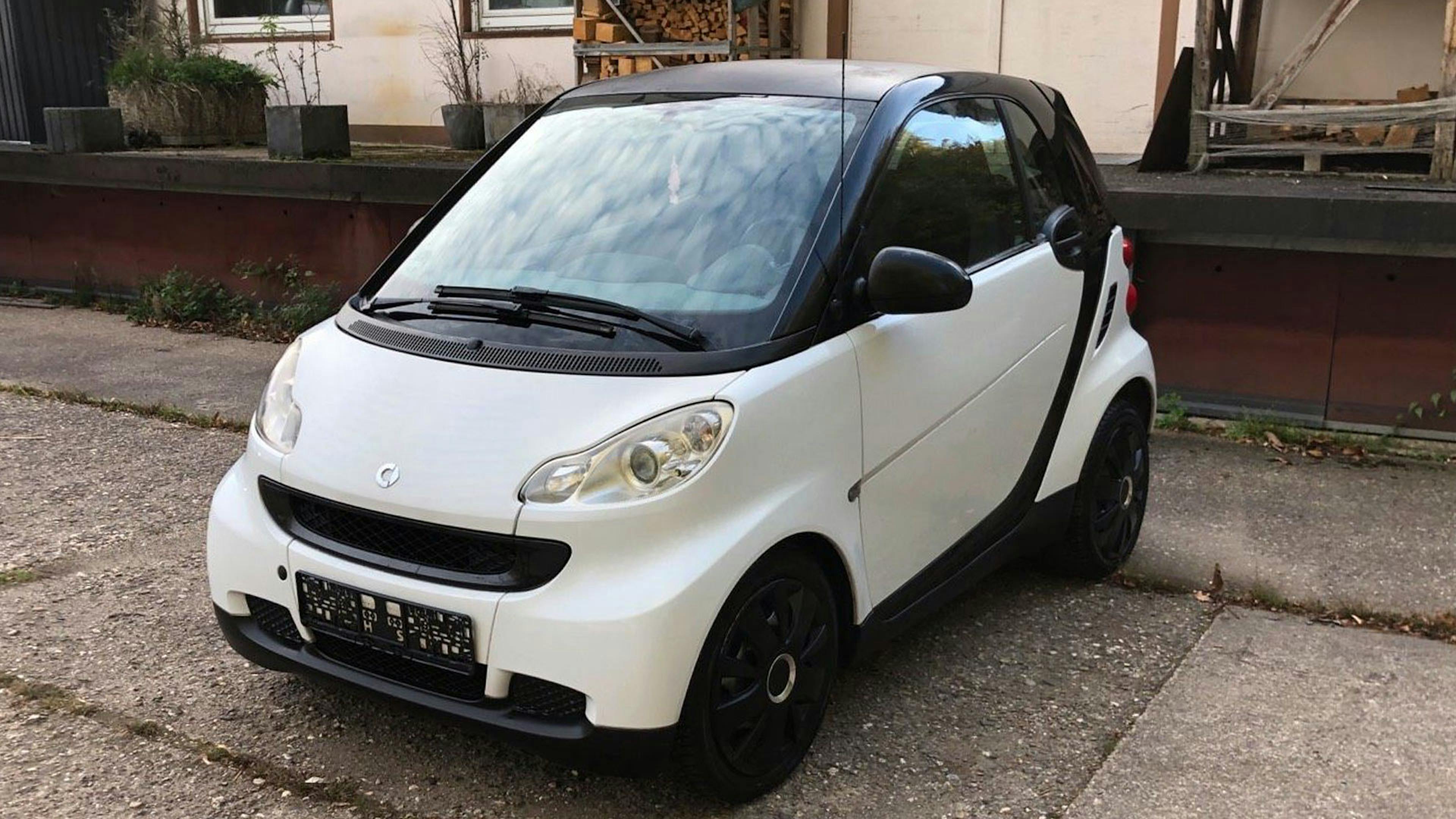 Ein schwarz-weißer Smart Fortwo steht vor einem Gebäude.