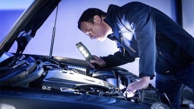 Ein Mechaniker leuchtet in den geöffneten Motorraum eines schwarzen Pkw