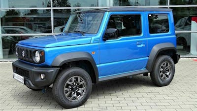 Ein blauer Suzuki Jimny steht vor einem Gebäude mit Fensterfront