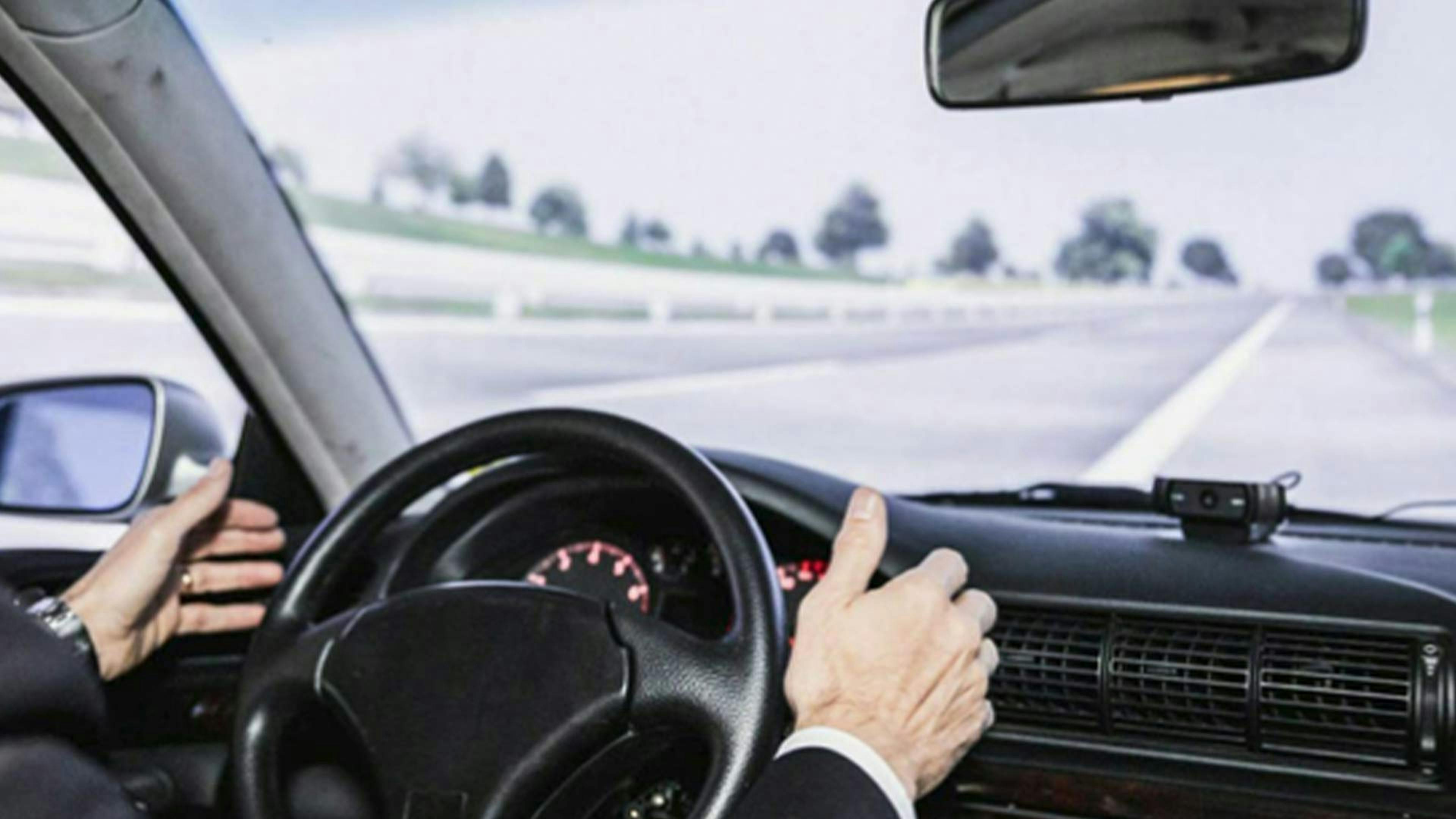 Eine Person sitzt am Steuer eines autonom fahrenden Pkw 