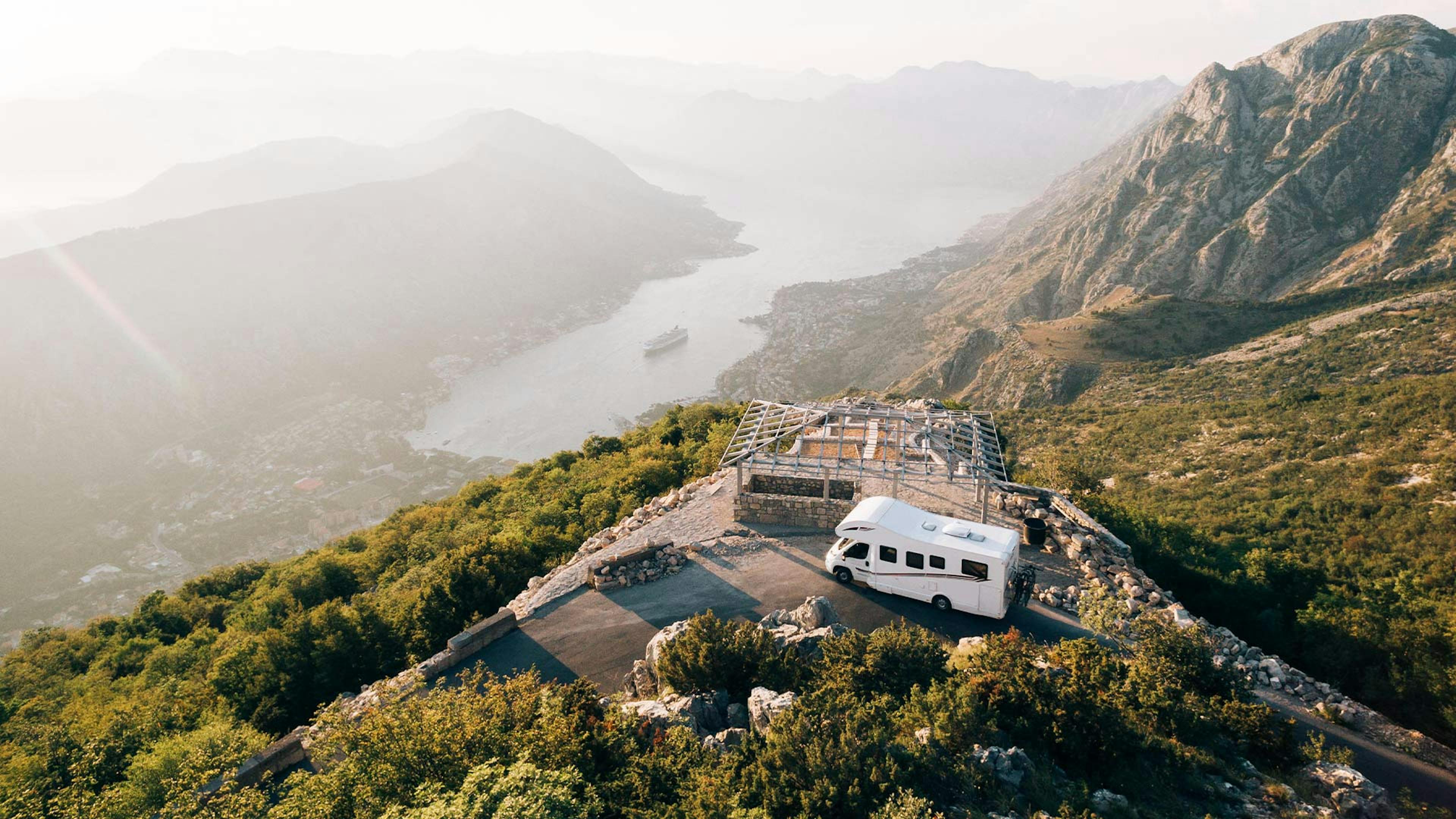 Luftaufnahme eines weißen Wohnmobils, das auf einem Berg in einer mediterranen Landschaft steht.