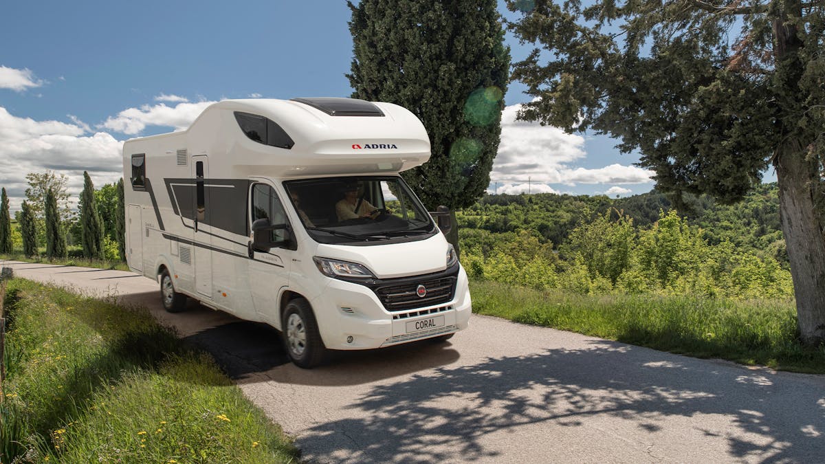Ein Coral XL Wohnmobil von Adria Mobile fährt eine Straße entlang durch eine mediterrane Landschaft.