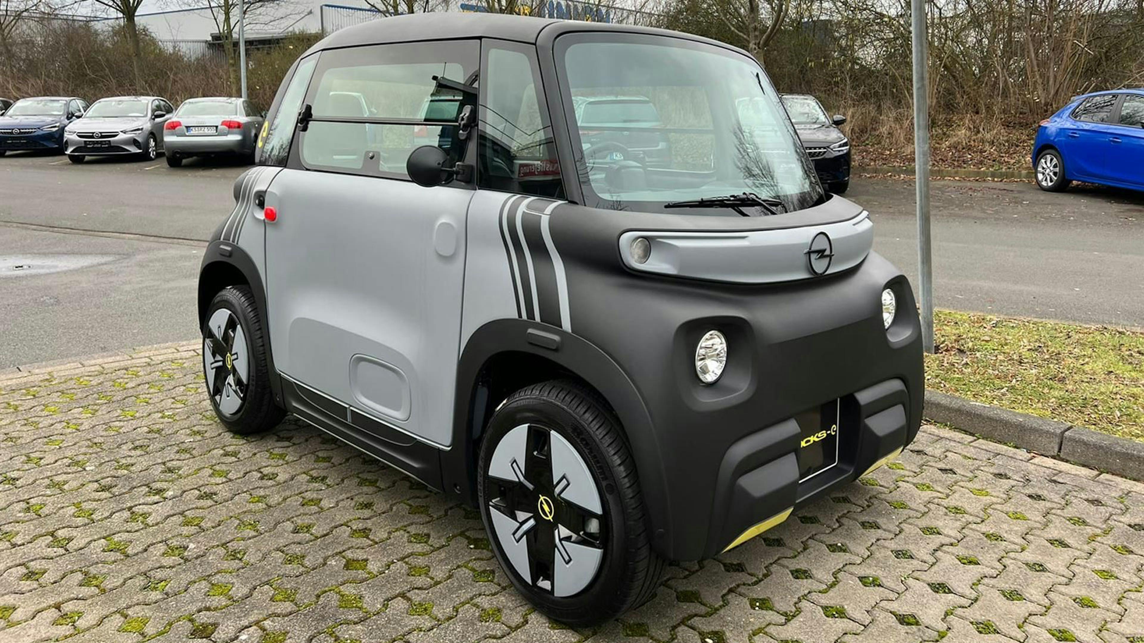 Ein grau-schwarzes Opel Rocks-e Microcar steht auf einem Parkplatz.