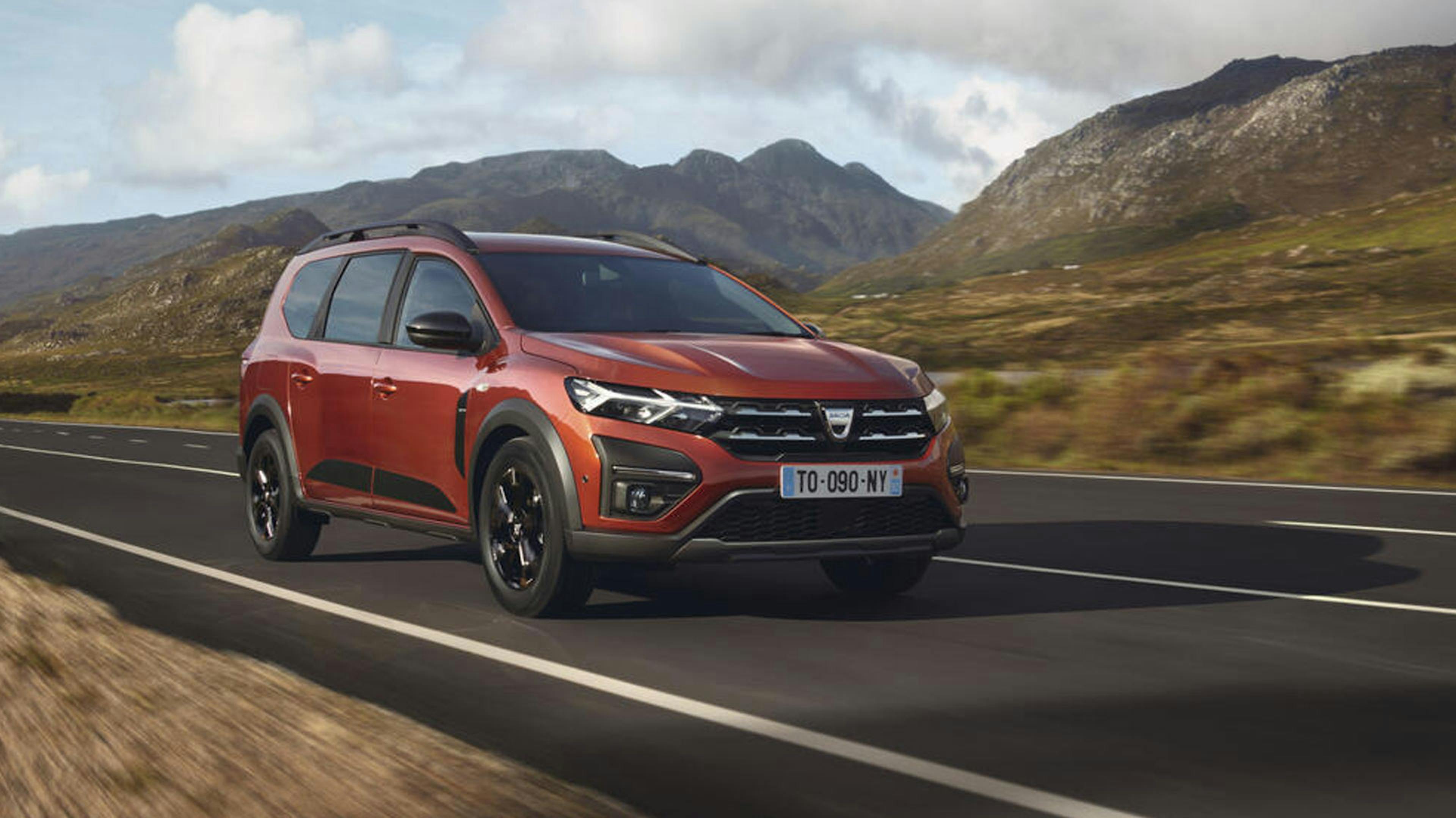 Ein roter Dacia Jogger mit Hybrid-Antrieb fährt eine Landstraße entlang.