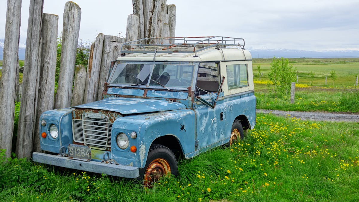 Ein kaputter blauer Land Rover steht vor einem Zaun auf einer Wiese