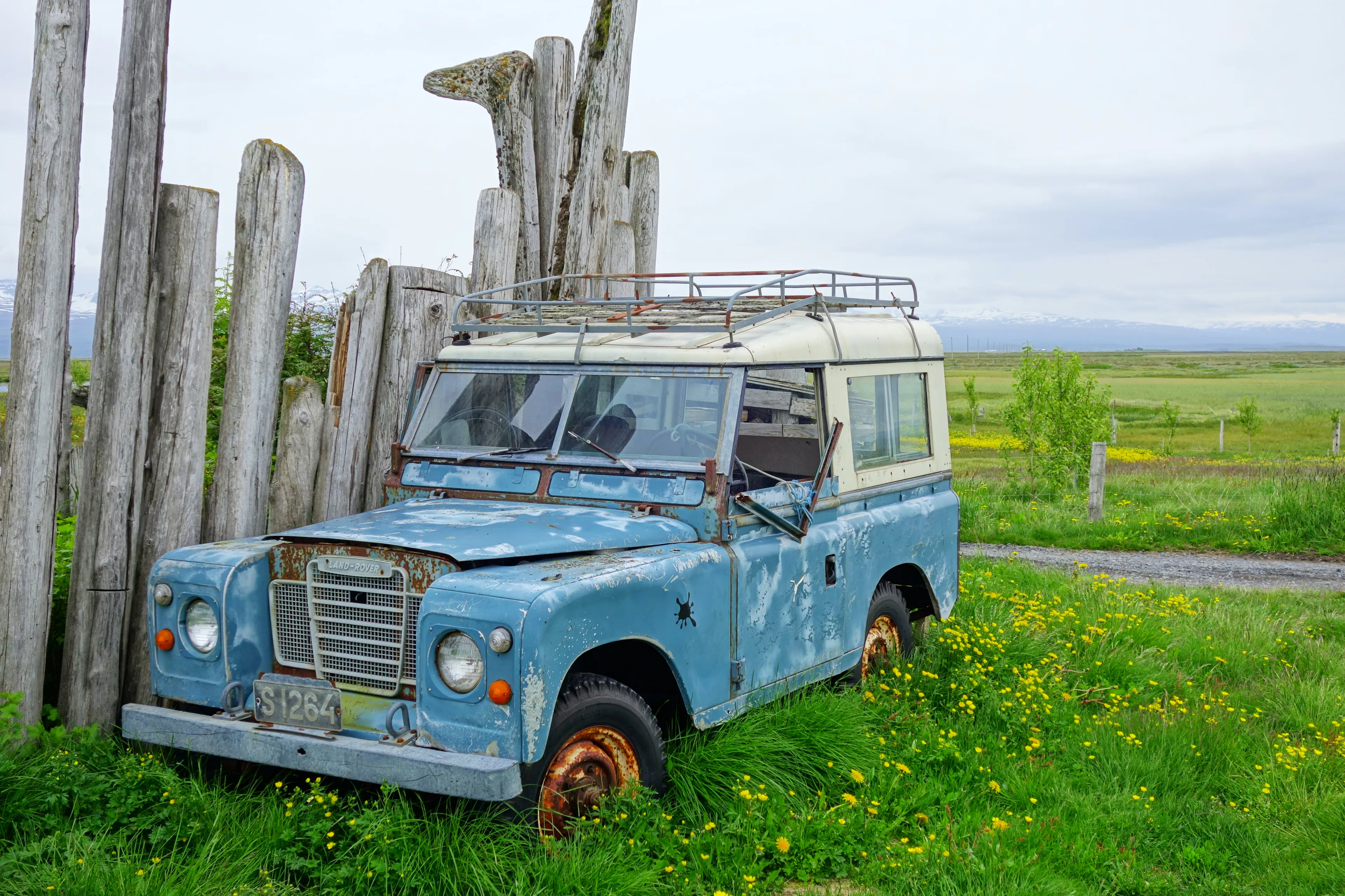Ein kaputter blauer Land Rover steht vor einem Zaun auf einer Wiese