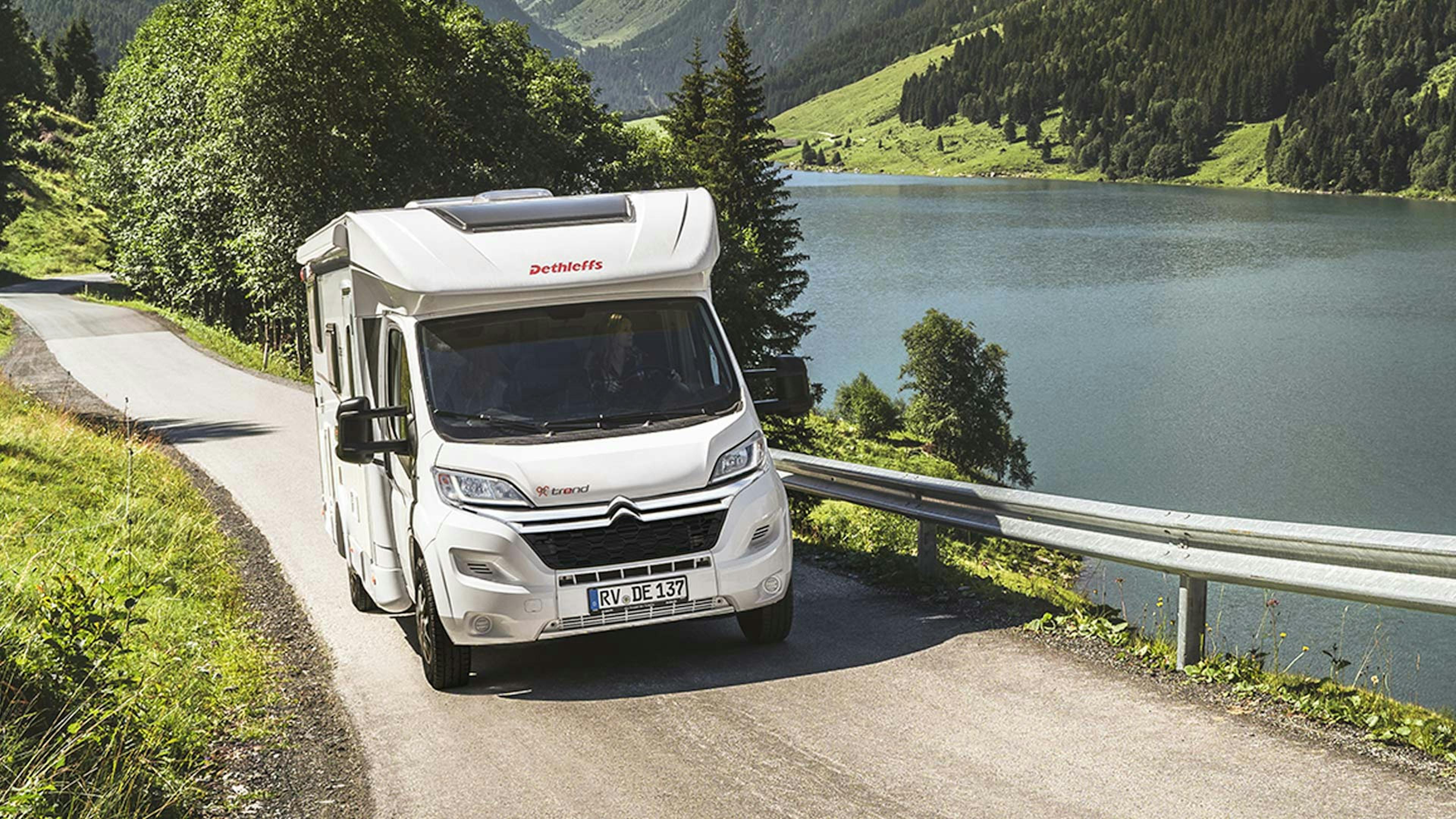 Ein Dethleffs Trend Wohnmobil mit Alkoven fährt an einem See vorbei.