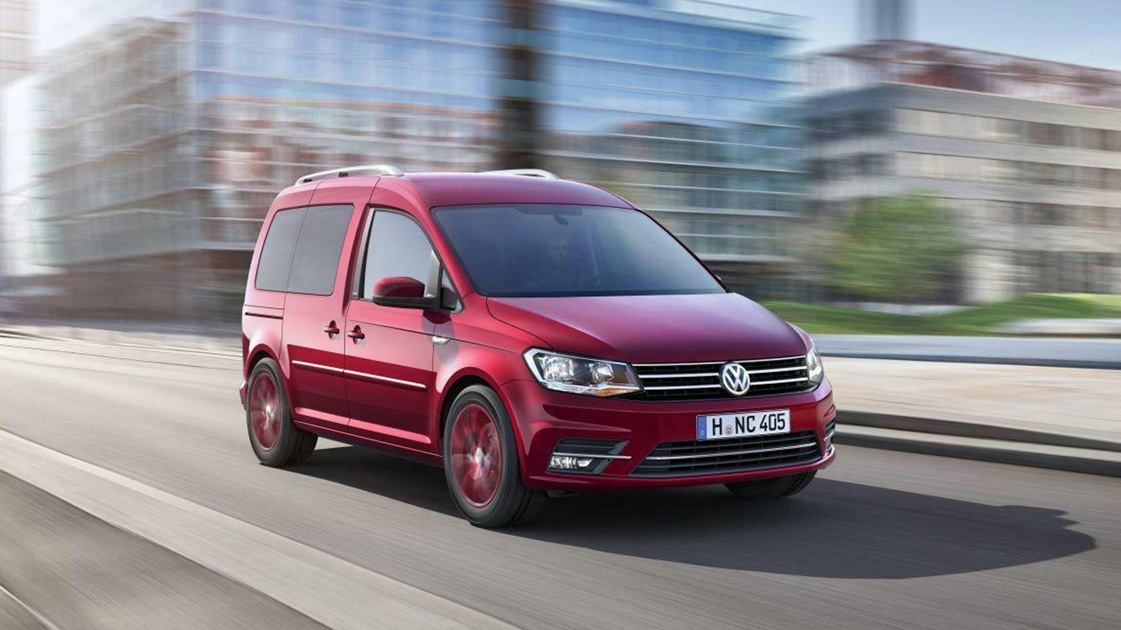 Ein roter VW Caddy Hochdachkombi fährt an einem grauen Gebäude vorbei.