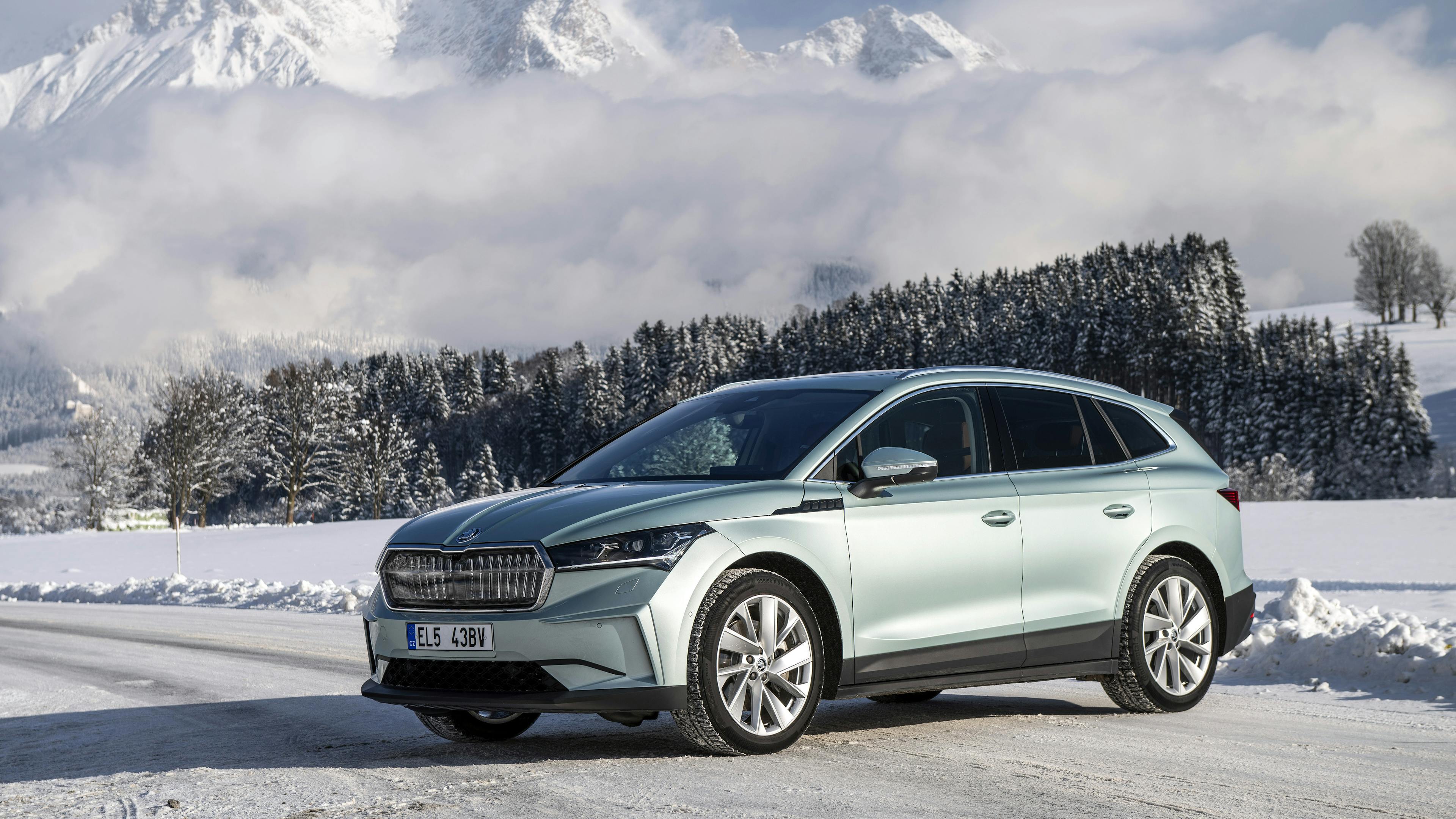 A green Skoda Enyaq is parked on a street in a wintry setting.