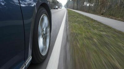 Detailaufnahme des rechten Vorderrads eines dunklen Pkw, der eine Landstraße entlang fährt