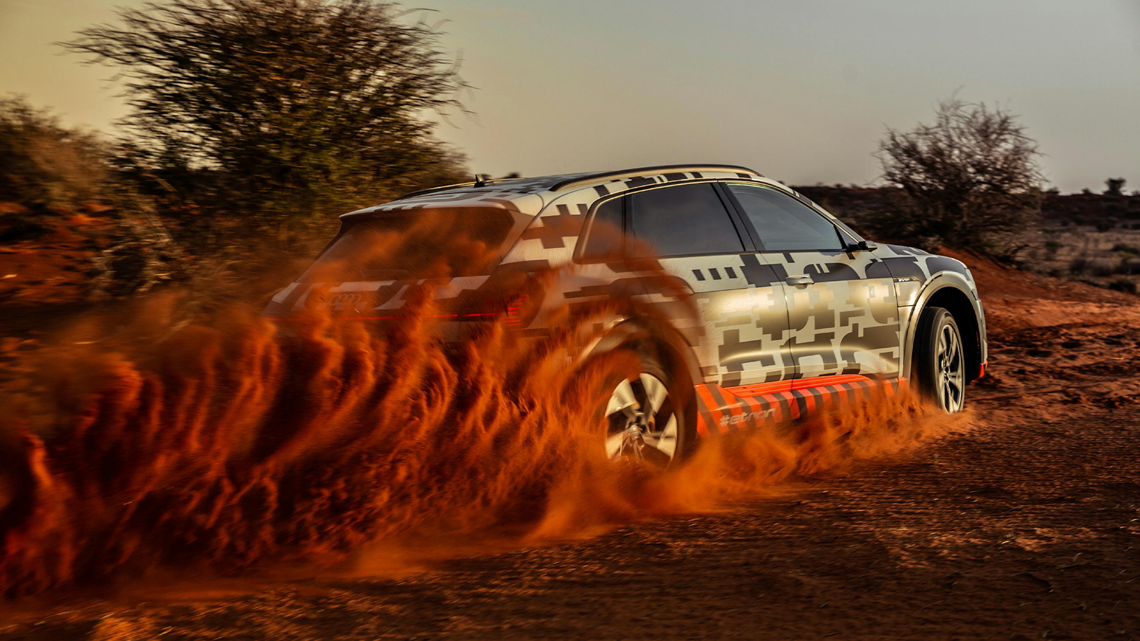 Ein schwarz-weißer Audi e-tron beschleunigt in einer wüstenartigen Landschaft.
