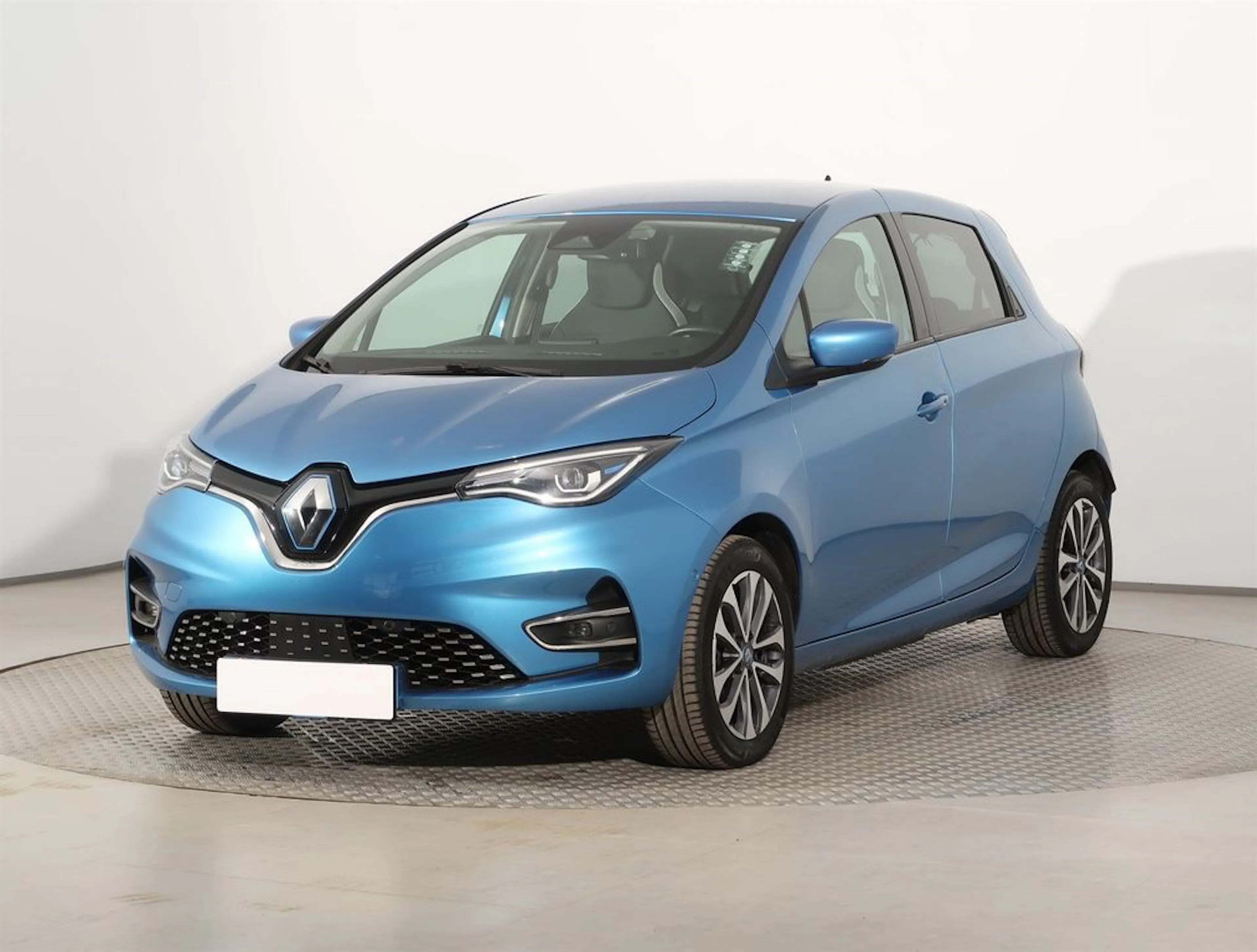 Blauer Renault Zoe, ein kompakter fünftüriger Elektro-Kleinwagen, steht in einem hellen Studio auf einer drehbaren Plattform.