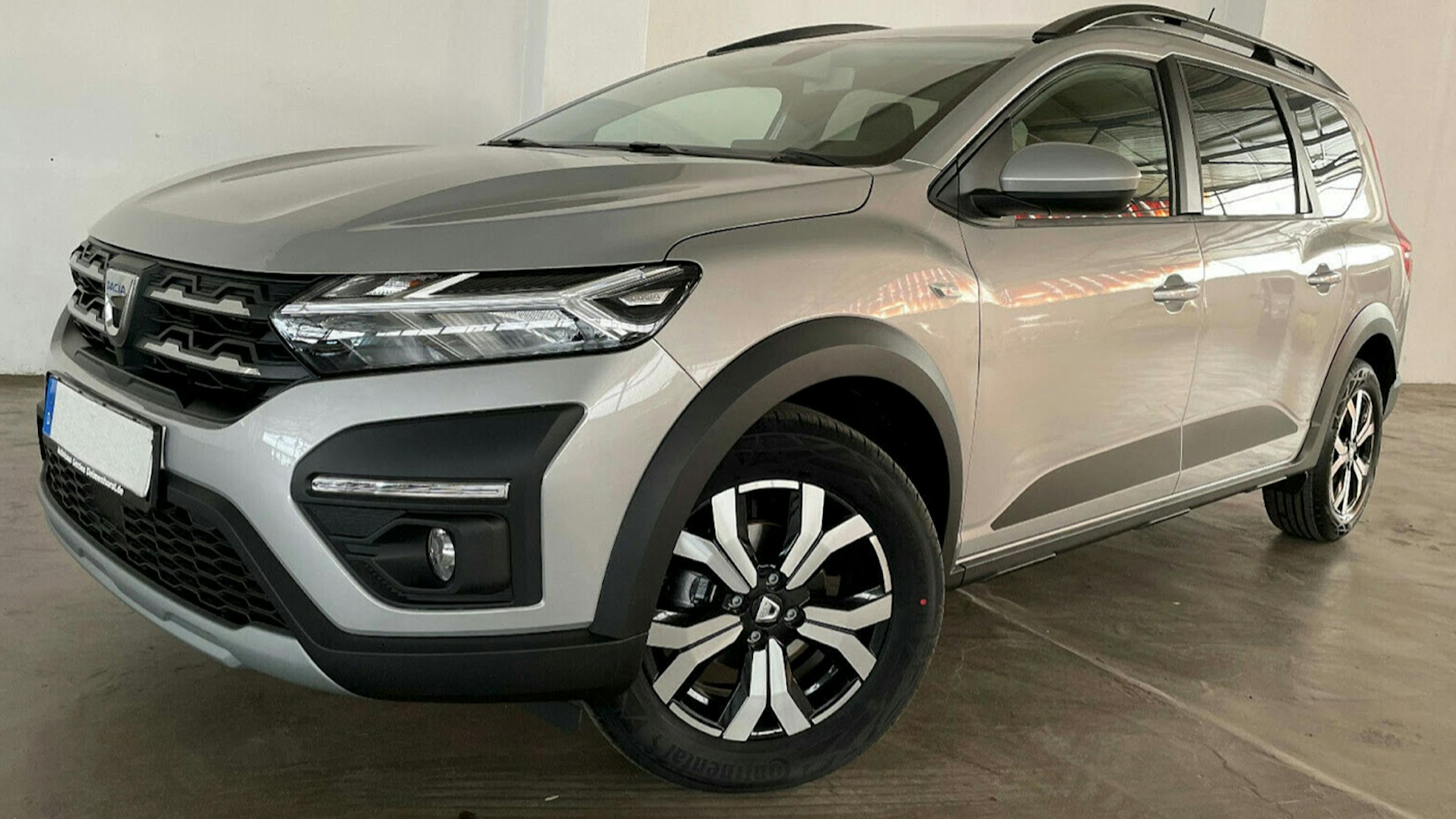 Ein silberner Dacia Jogger Hochdachkombi steht vor einer weißen Wand.