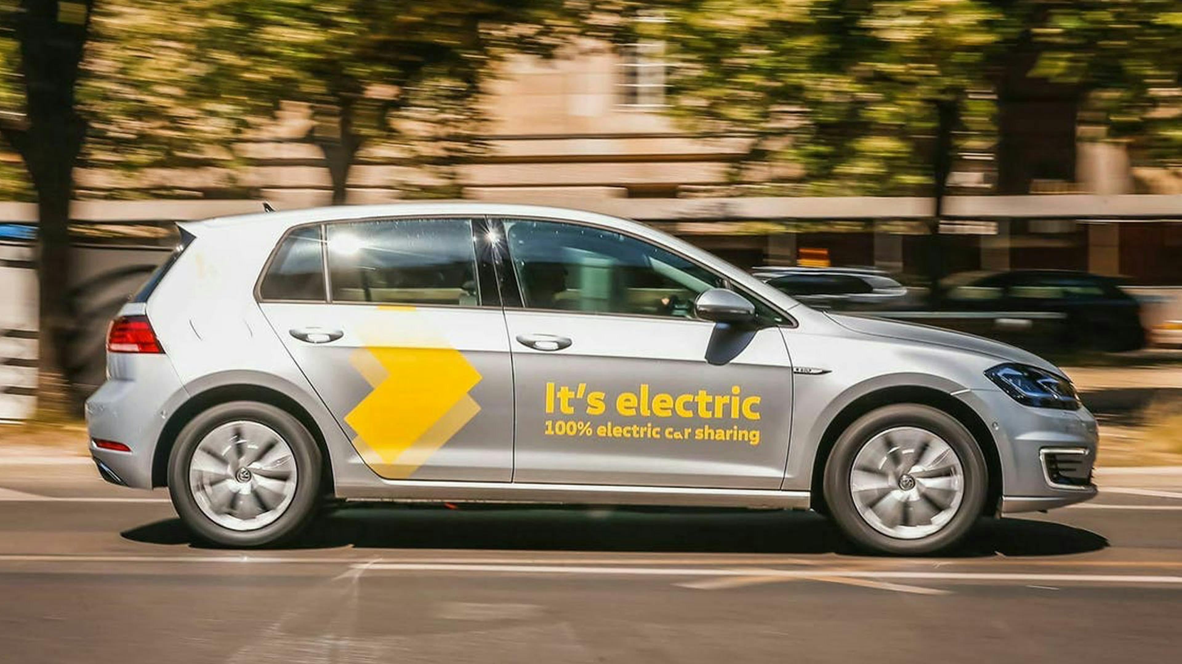 Ein silberner Pkw einer Carsharing-Flotte fährt durch eine urbane Kulisse.