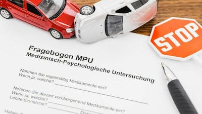 Stillleben mit einem MPU-Fragebogen, zwei Spielzeugautos, einem Stoppschild und einem Kugelschreiber