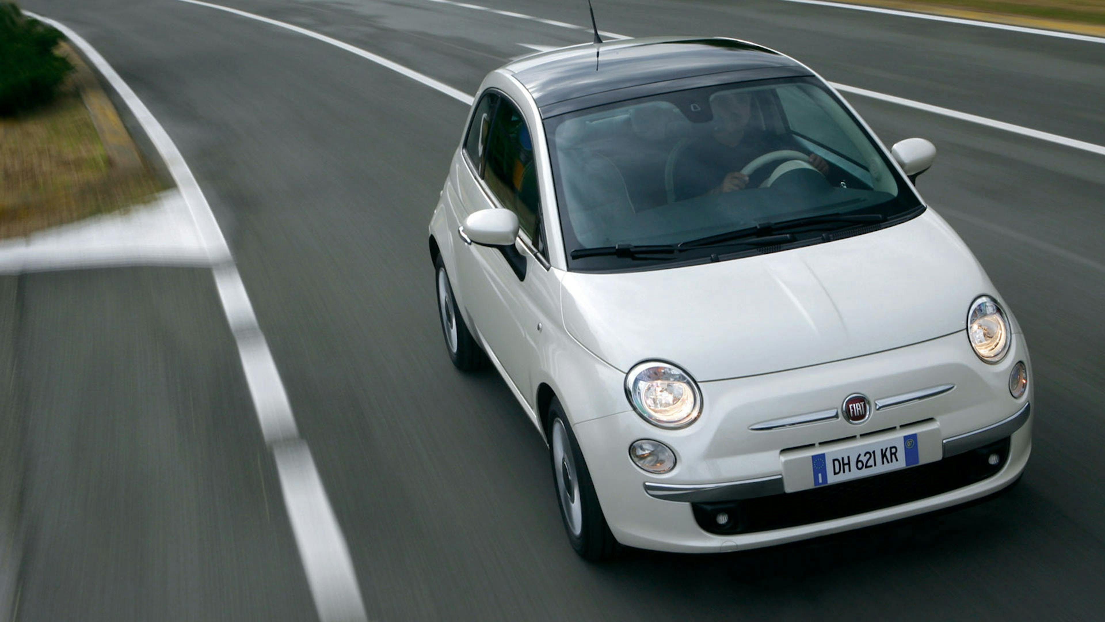 Ein silberner Fiat 500 Kleinstwagen fährt eine Straße entlang.