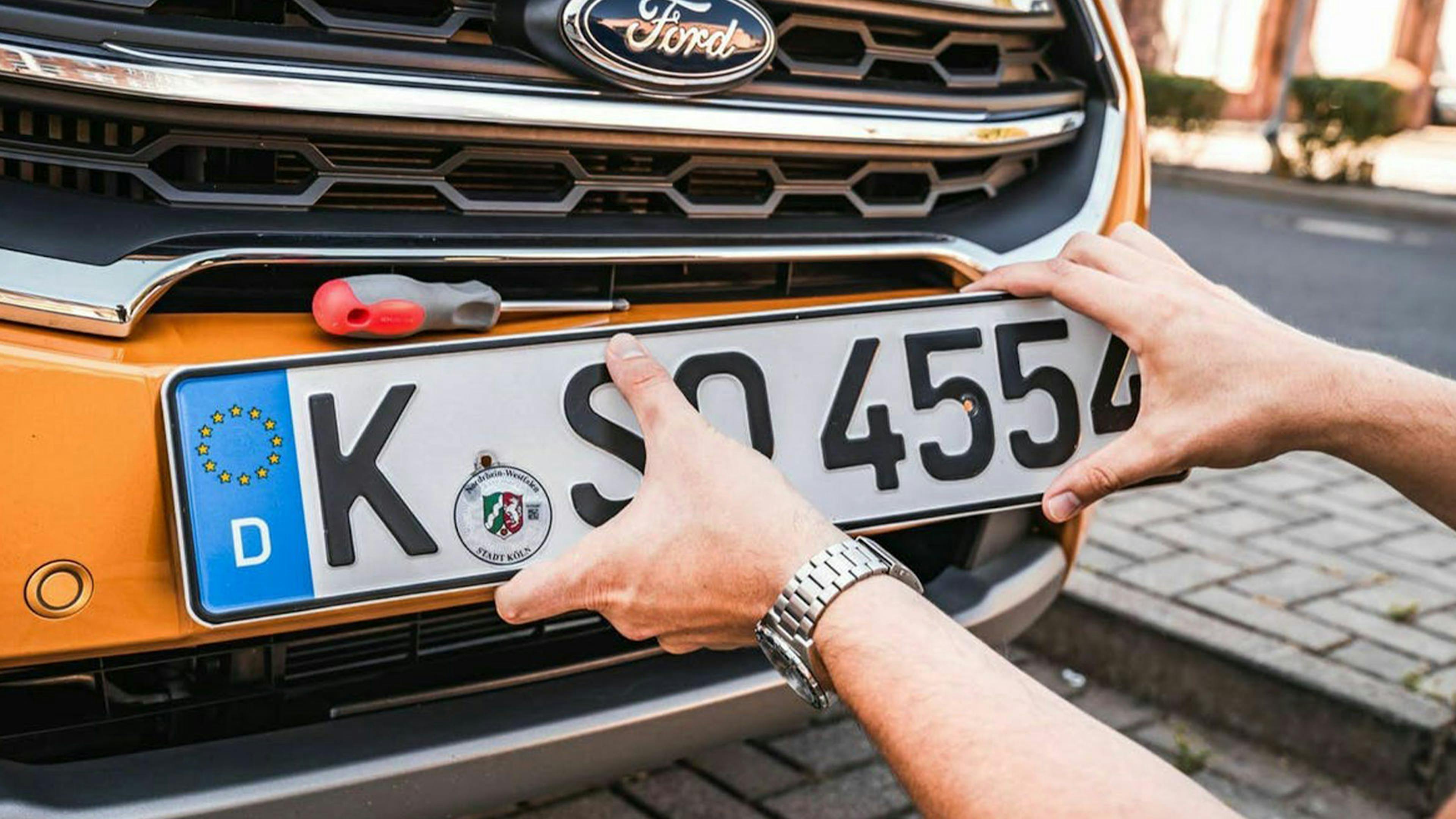 Ein Nummernschild wird von einem orangefarbenen Pkw abmontiert