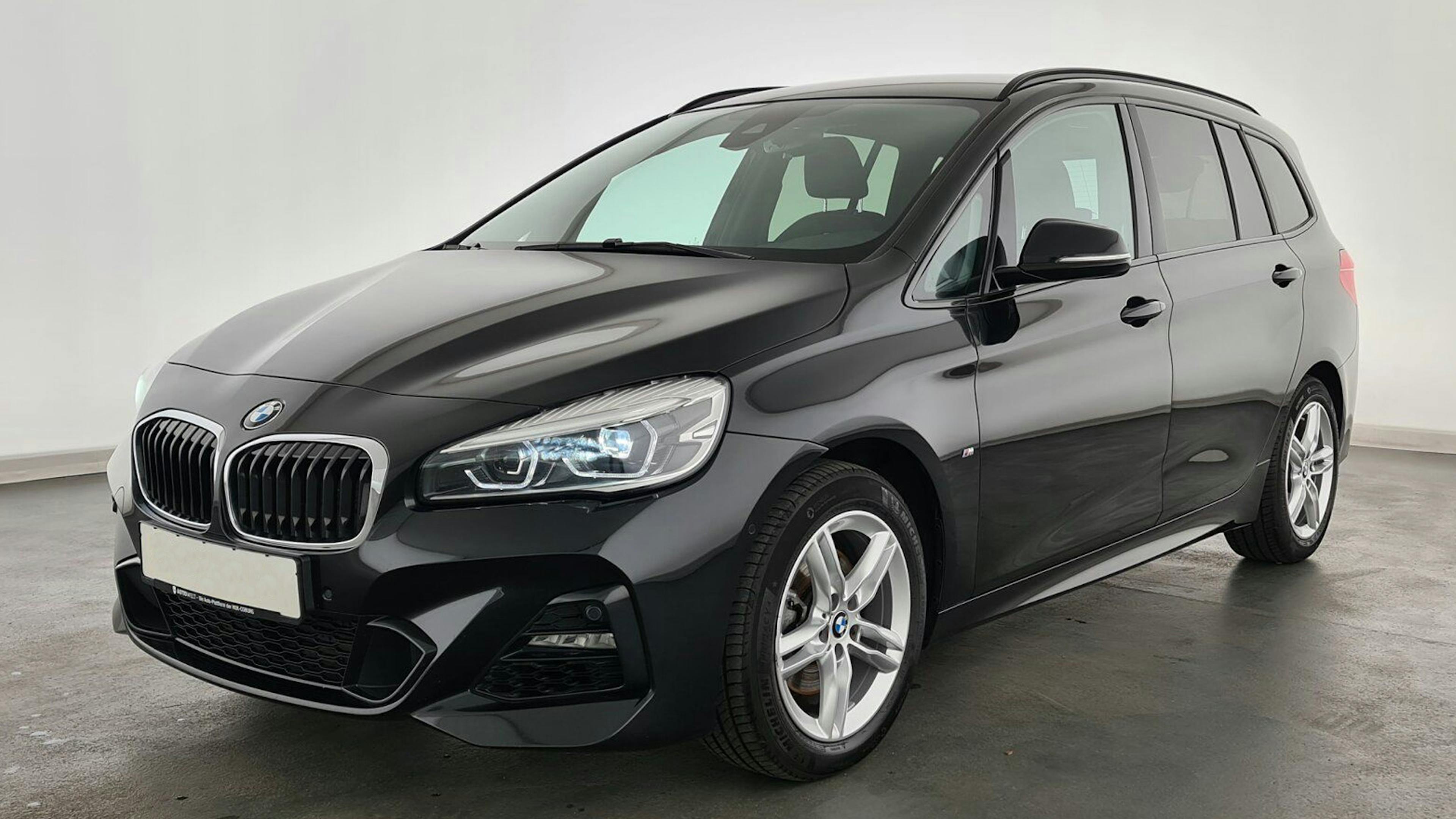 Ein schwarzer BMW 2er Gran Tourer steht vor einer weißen Wand.