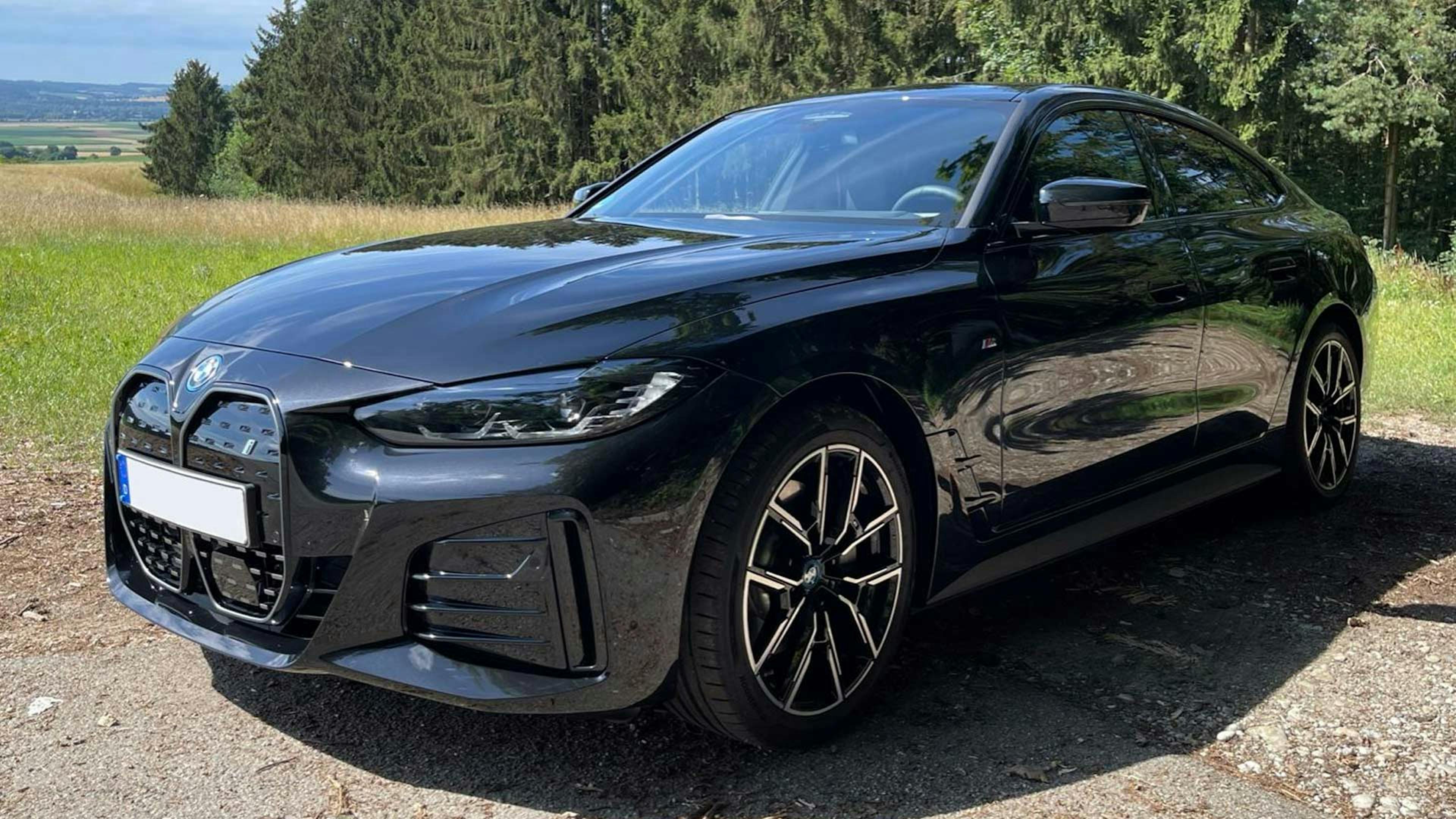 Ein schwarzer BMW i4 steht an einem Waldrand.