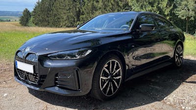 Ein schwarzer BMW i4 steht an einem Waldrand.