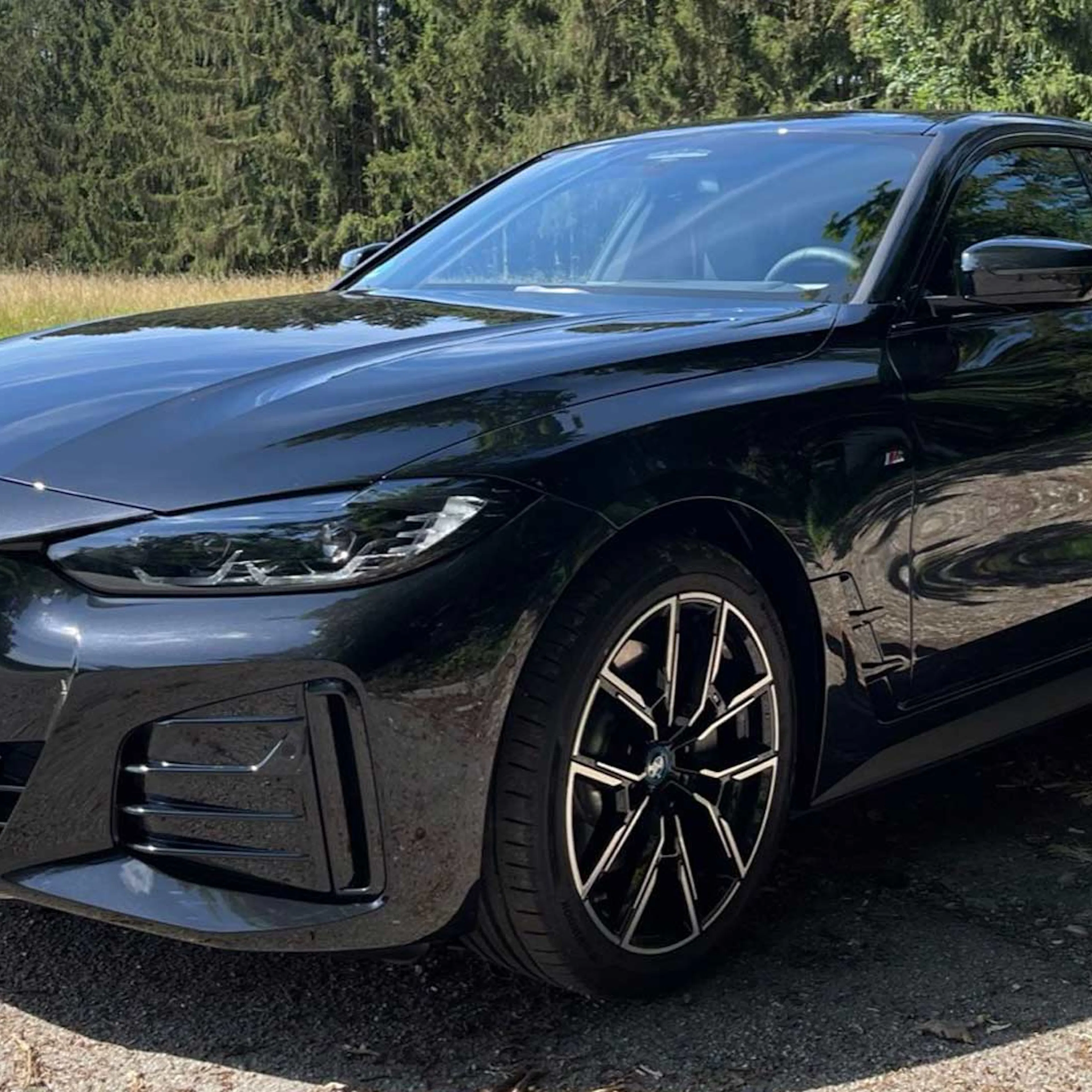 Ein schwarzer BMW i4 steht an einem Waldrand.