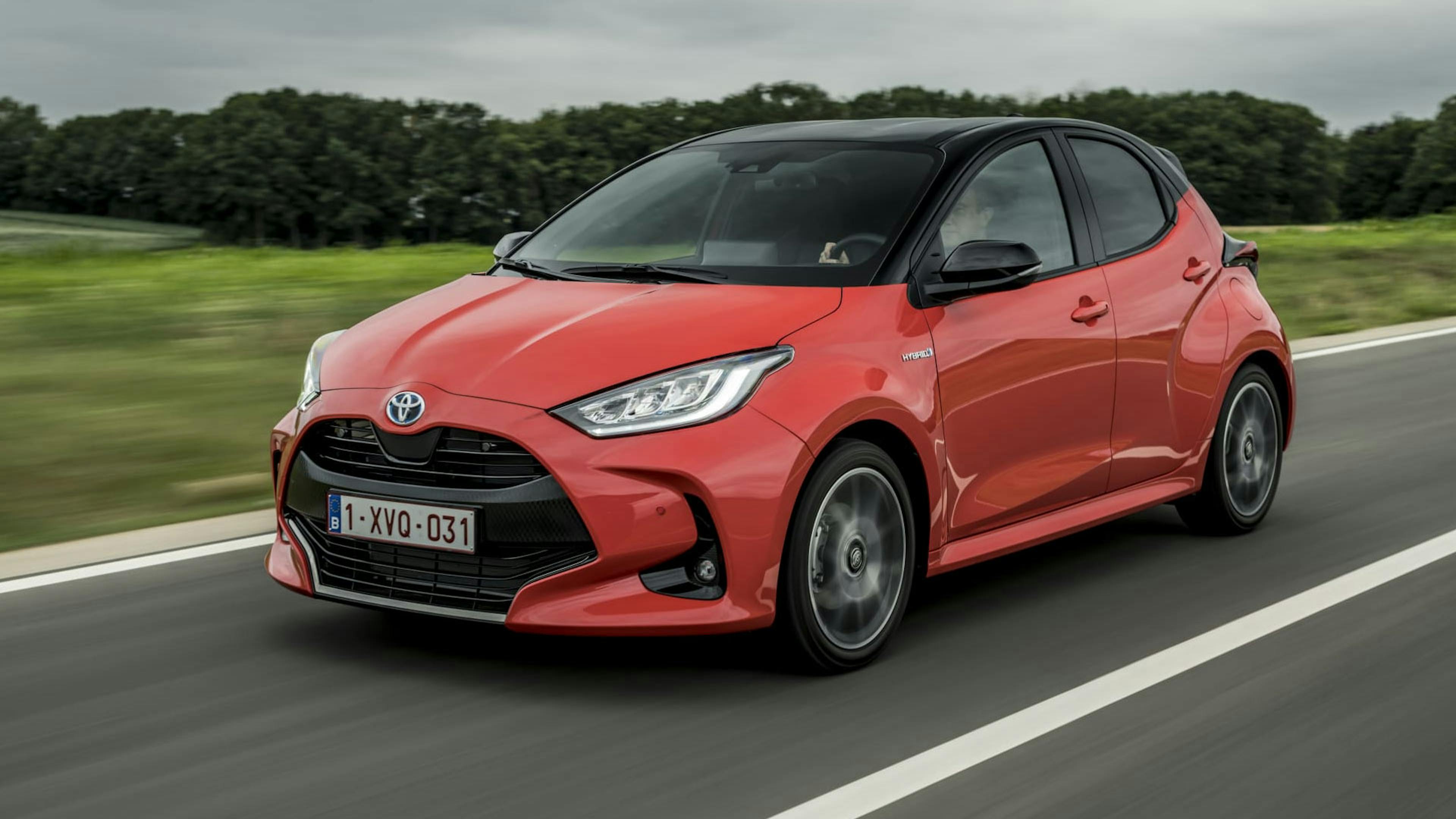 Ein roter Toyota Yaris Hybrid fährt eine Landstraße entlang.