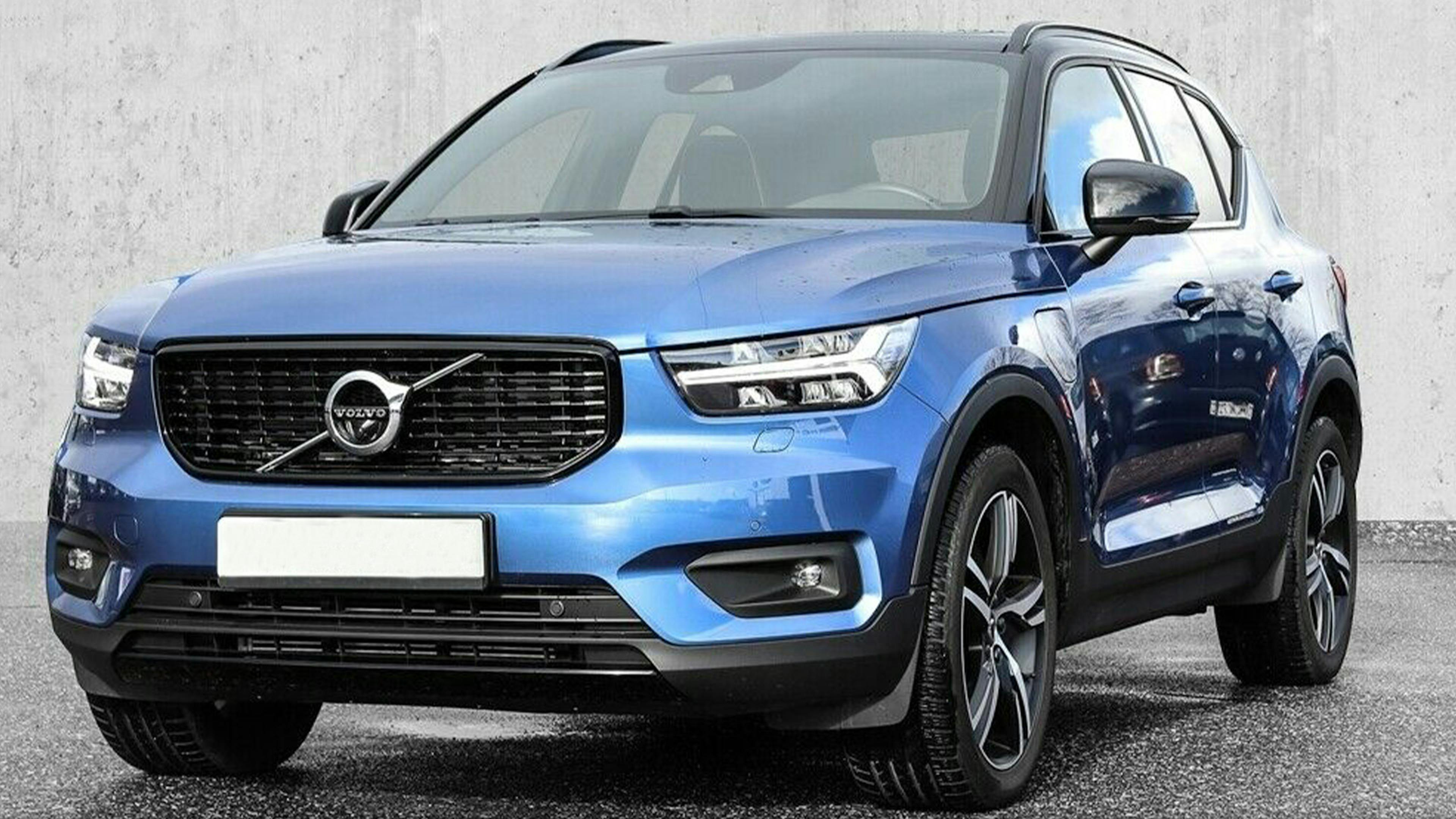 Ein blauer Volvo XC40 Recharge mit Anhängerkupplung steht vor einer grauen Wand