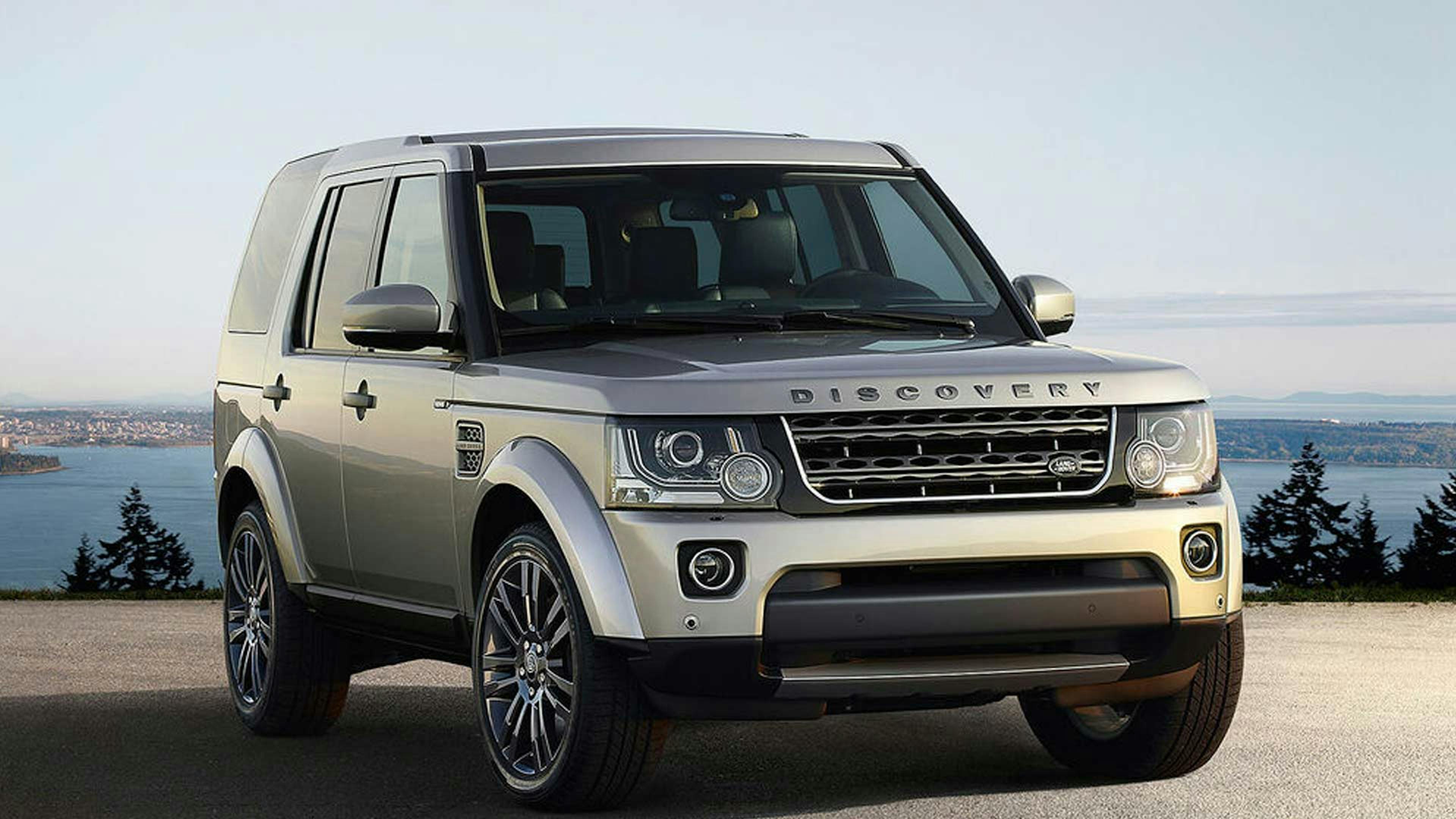 Ein silberner Land Rover Discovery 4 steht auf einer Anhöhe vor einem Gewässer.