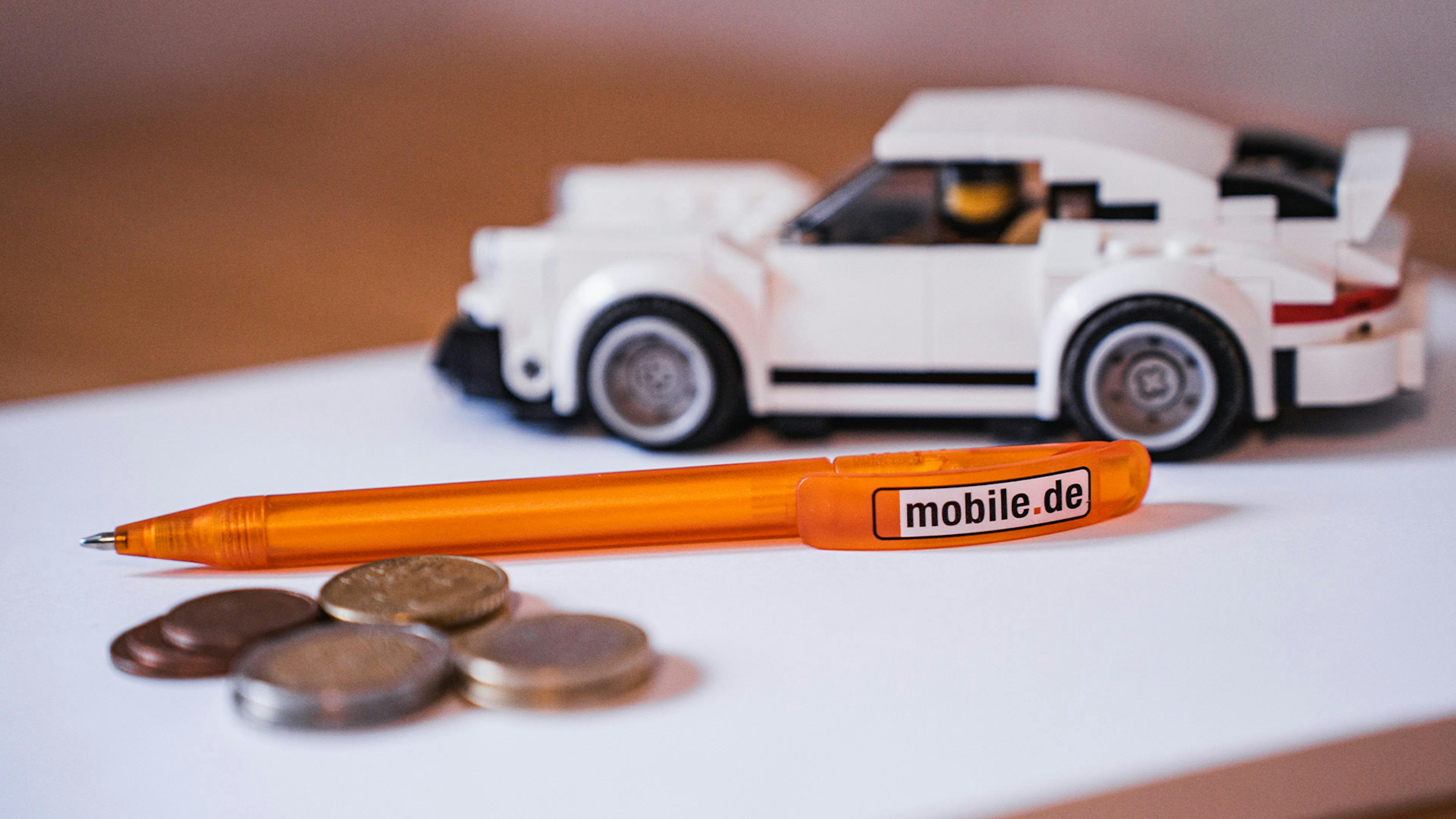 Symbolbild zum Thema Autoverkauf mit einem Spielzeugauto, Euro-Münzen und einem Kugelschreiber.