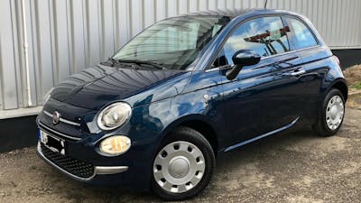 Ein blauer Fiat 500 steht vor einem grauen Rolltor.