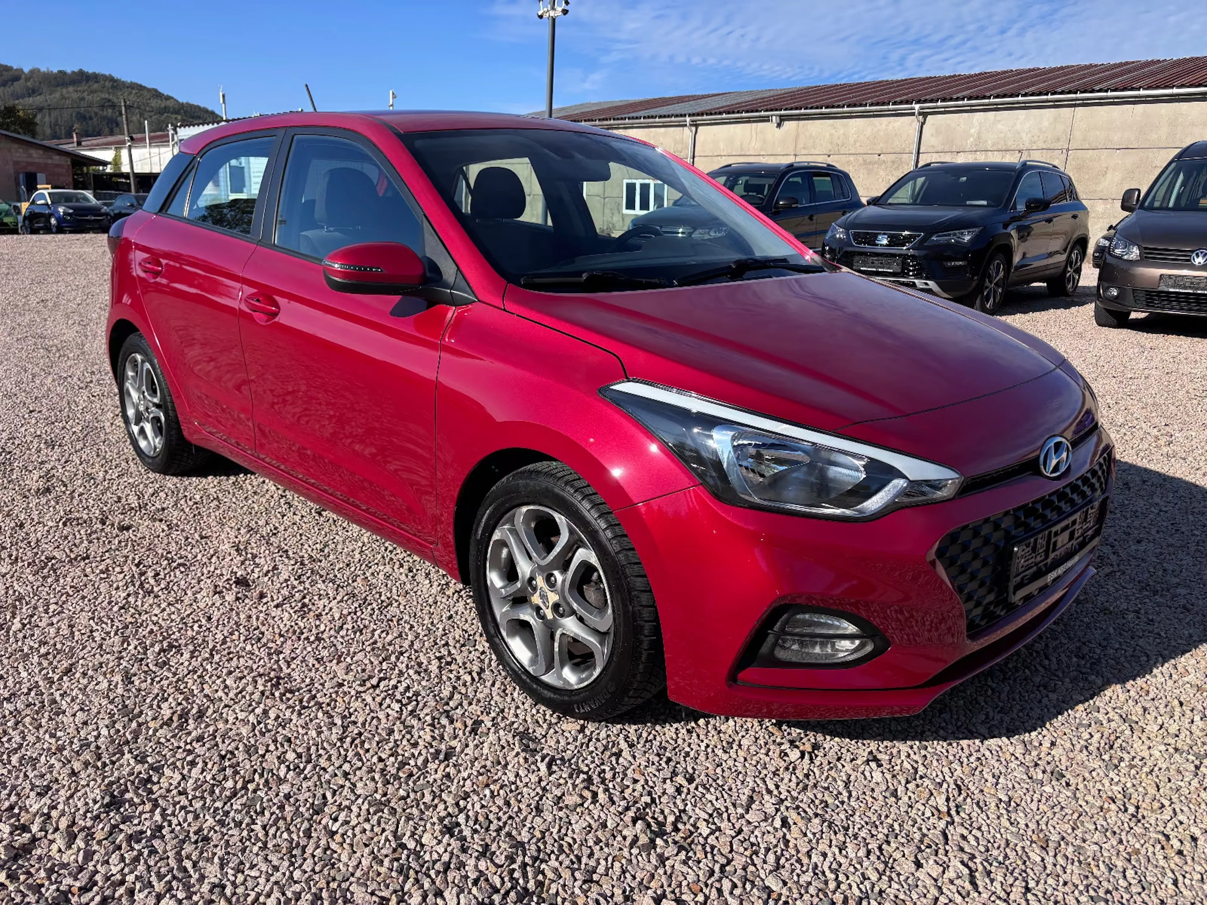 Ein roter Hyundai i20 steht auf einer Kiesfläche.