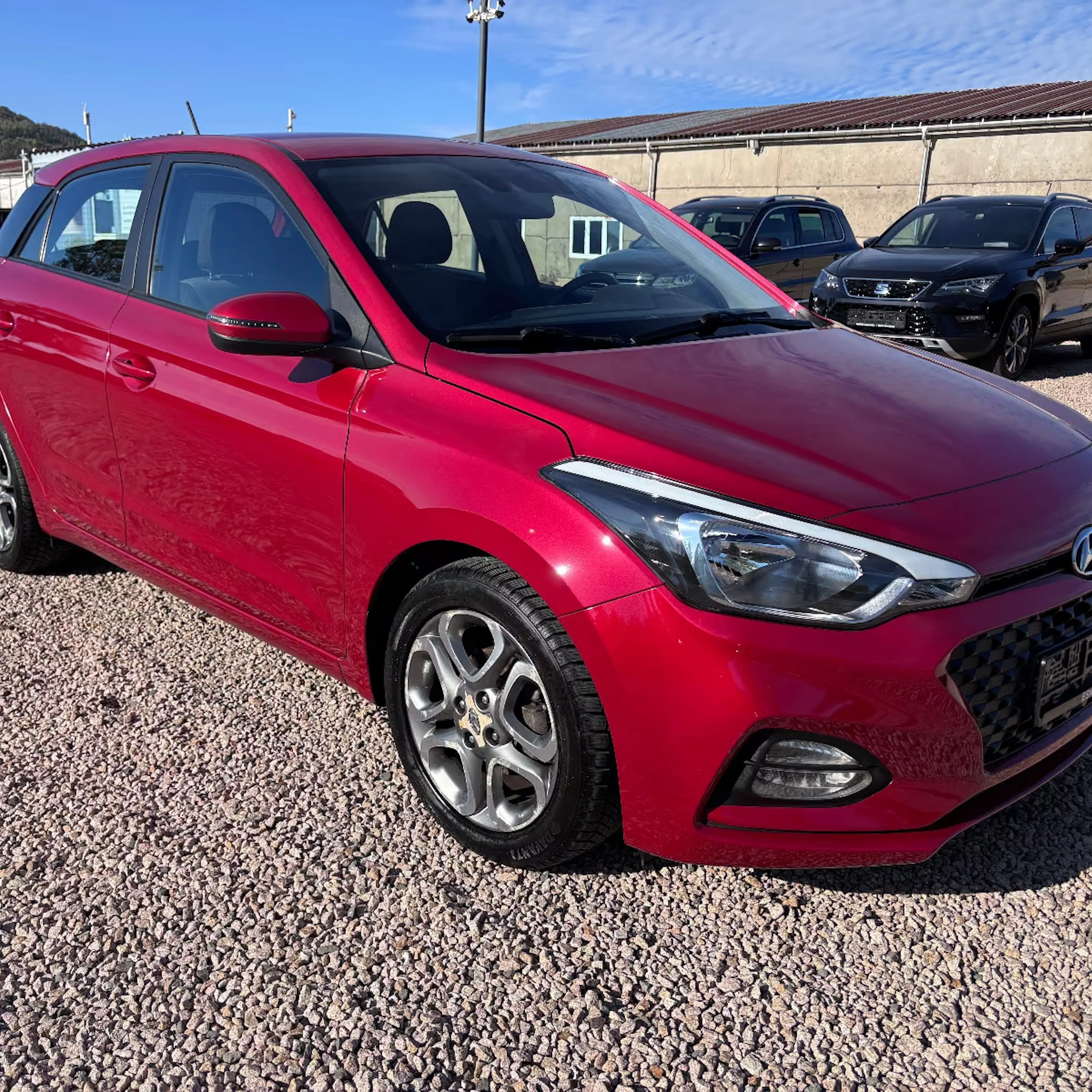 Ein roter Hyundai i20 steht auf einer Kiesfläche.