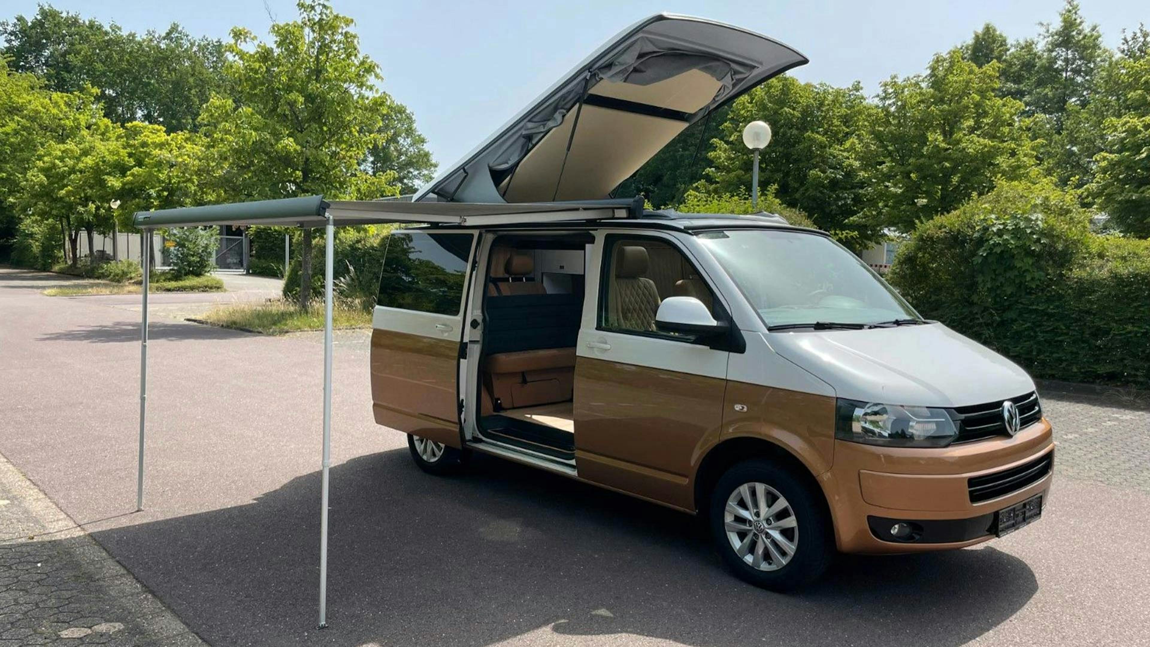 Ein braun-weißer VW California Camper steht auf einem Parkplatz.