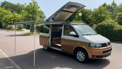 Ein braun-weißer VW California Camper steht auf einem Parkplatz.