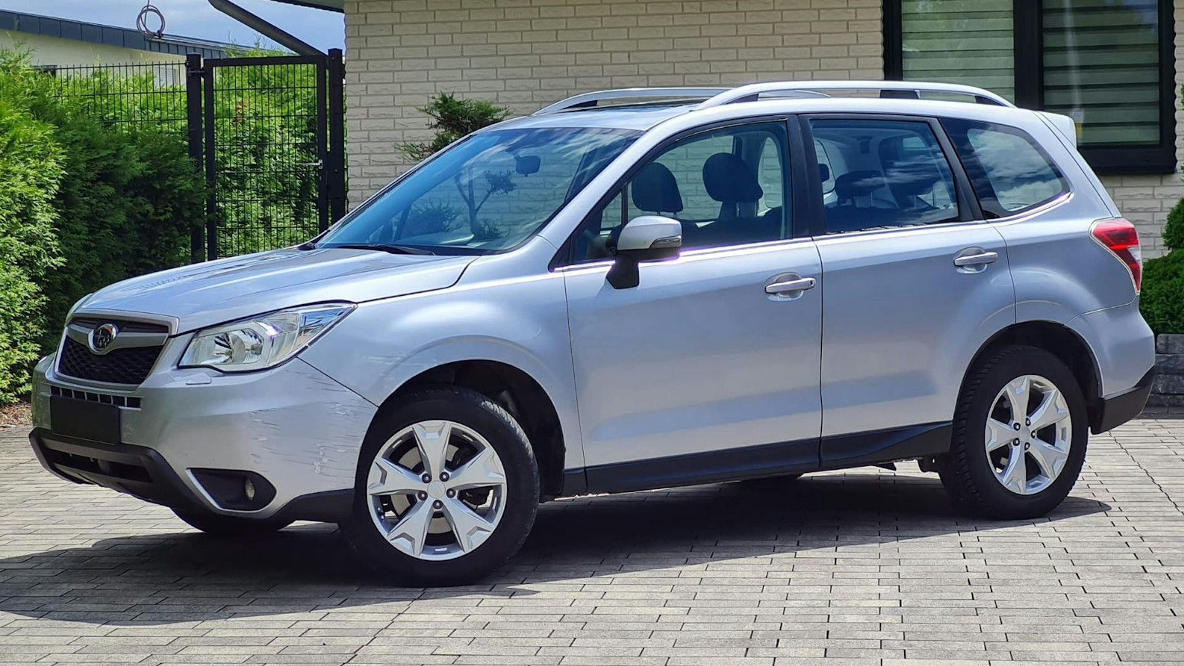 Ein weißer Subaru Forester Geländewagen steht vor einem Haus mit heller Fassade.