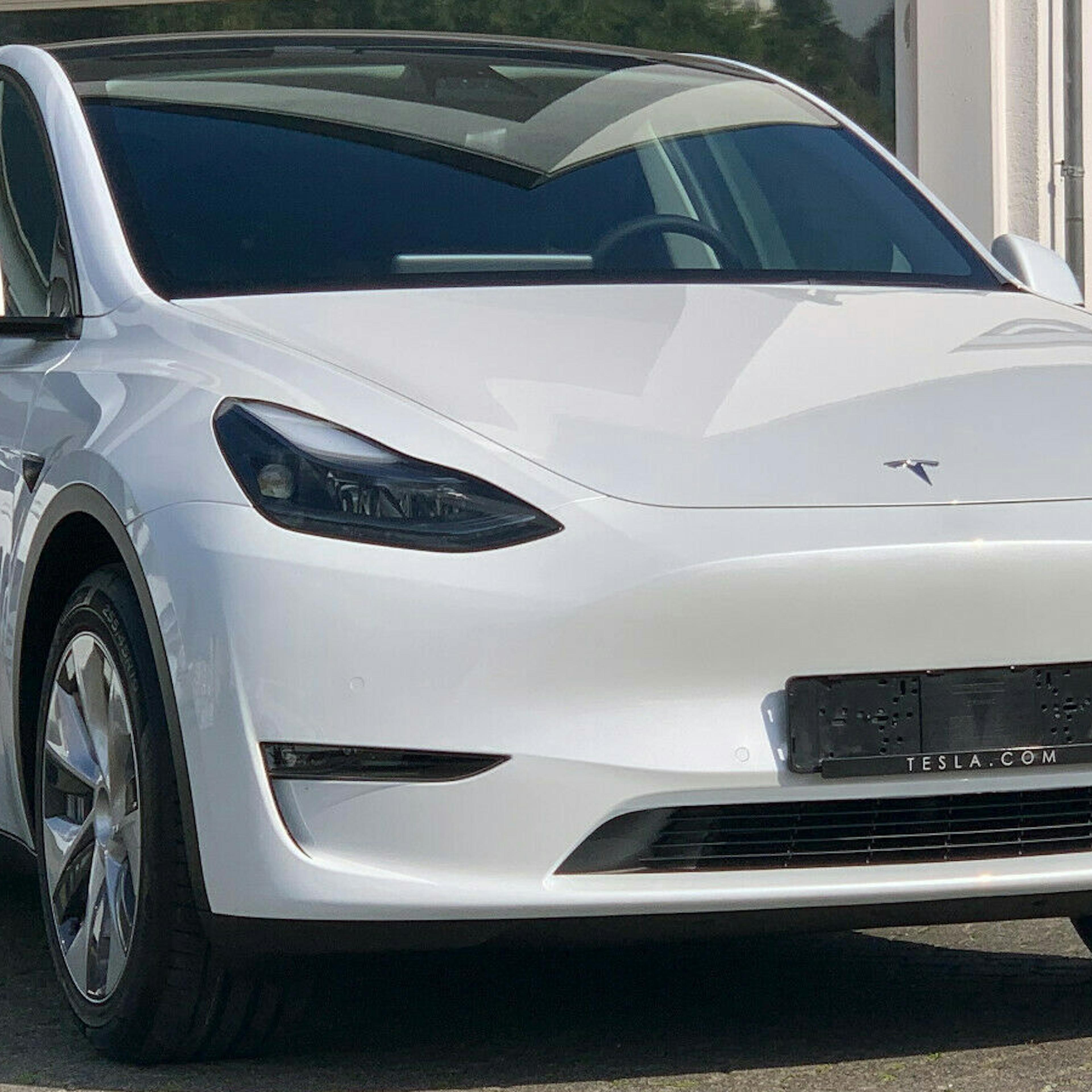 Ein weißes Model Y von Tesla mit Anhängerkupplung steht vor einem weißen Gebäude