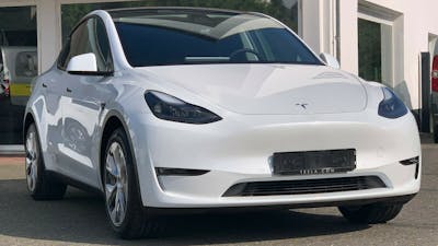 Ein weißes Model Y von Tesla mit Anhängerkupplung steht vor einem weißen Gebäude