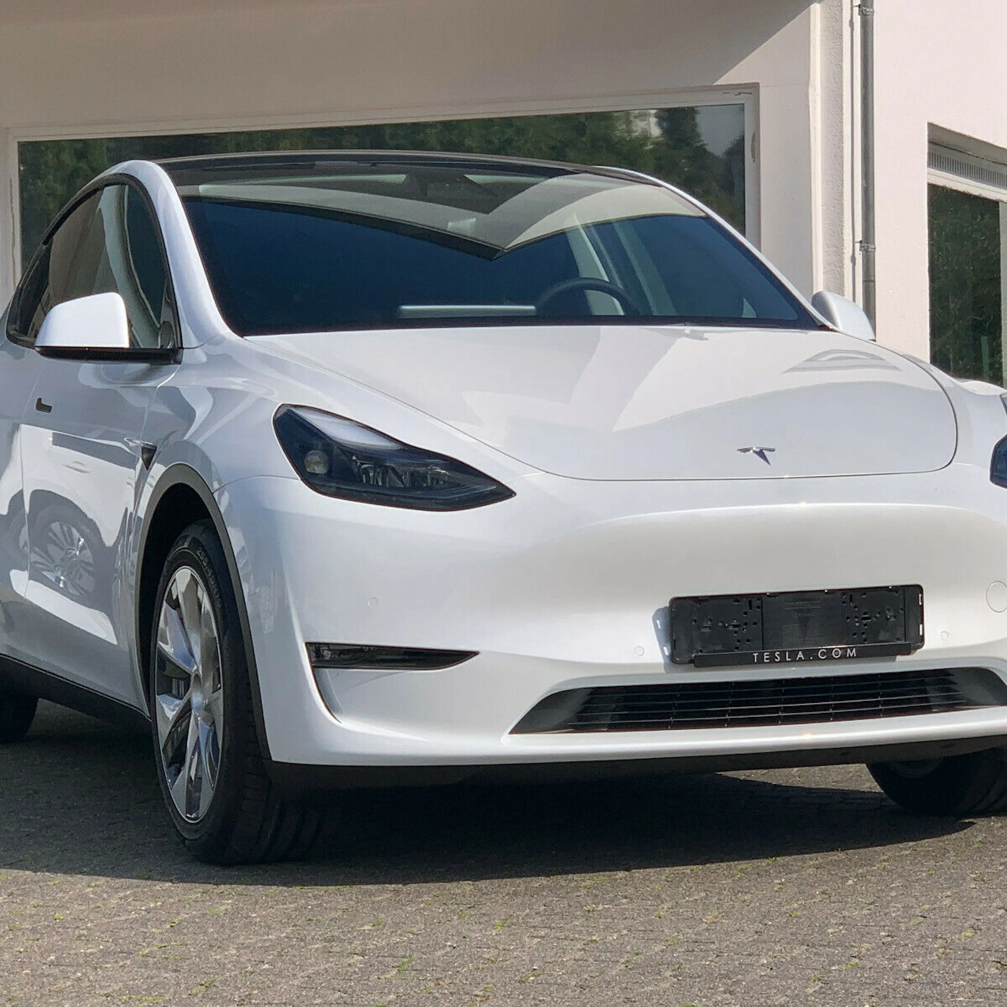 Ein weißes Tesla Model Y steht vor einem Gebäude mit weißer Fassade.