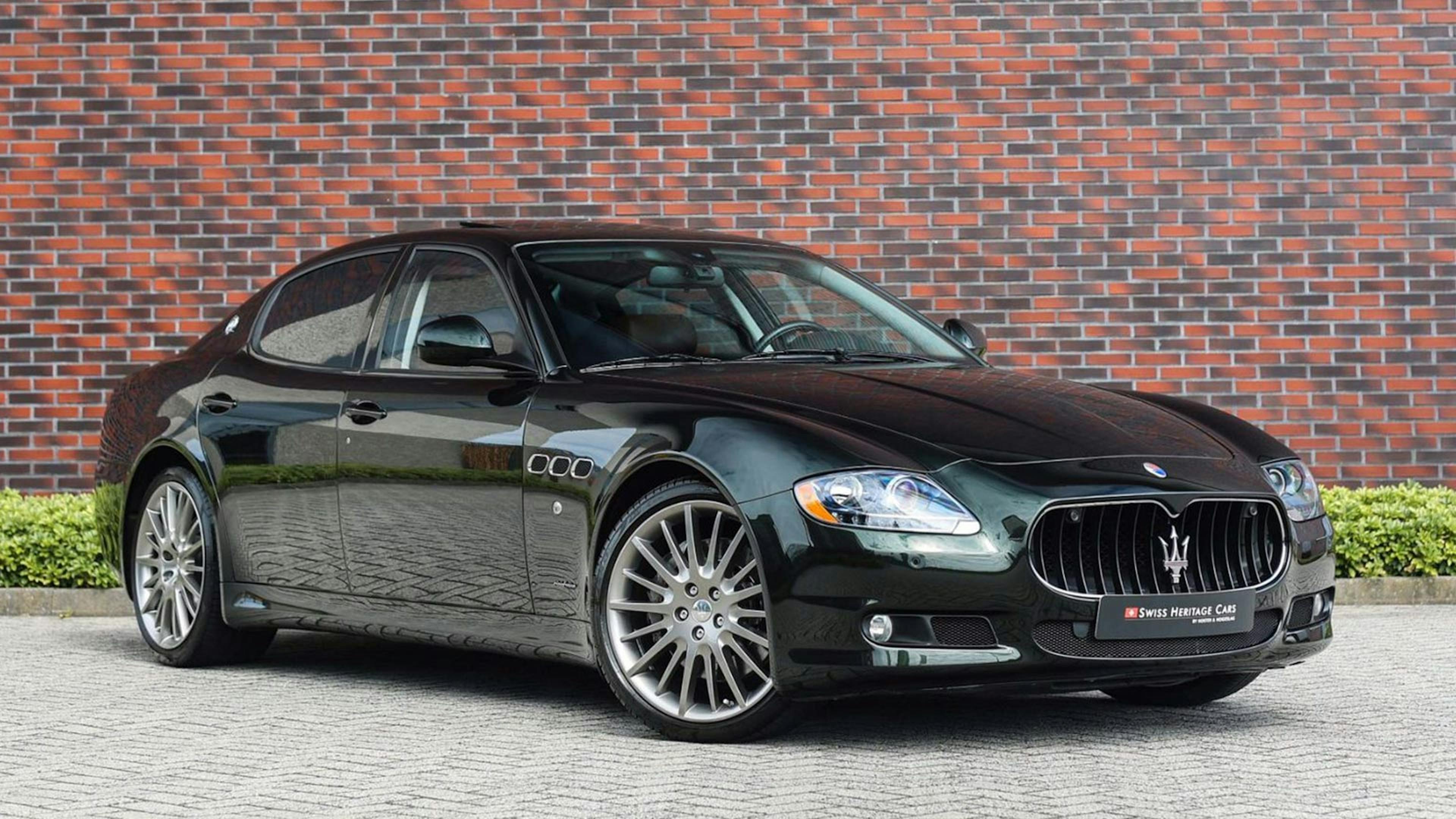 Ein schwarzer Maserati Quattroporte steht vor einer Backsteinwand.