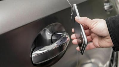 Eine Person öffnet ein graues Auto mithilfe eines Smartphones